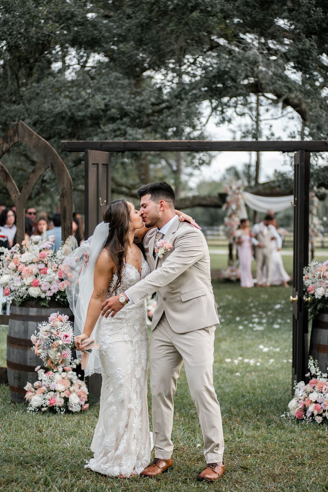 A wedding celebration in an outdoor garden setting with pink floral arrangements and white petals.