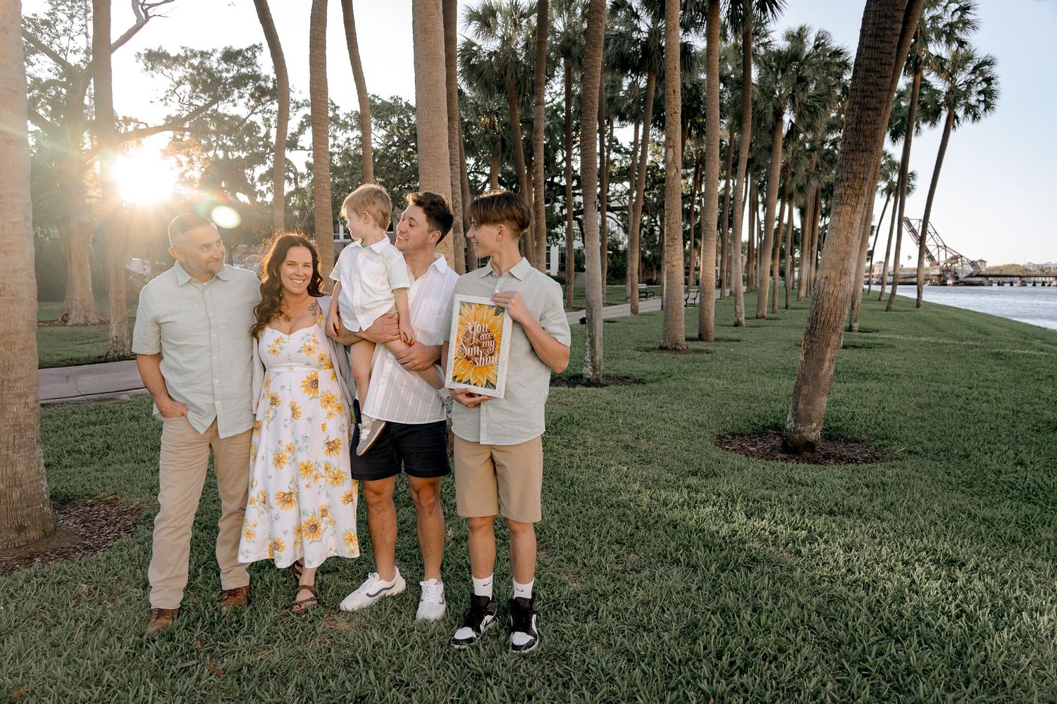 Family gathering at sunset among palm trees near waterfront.