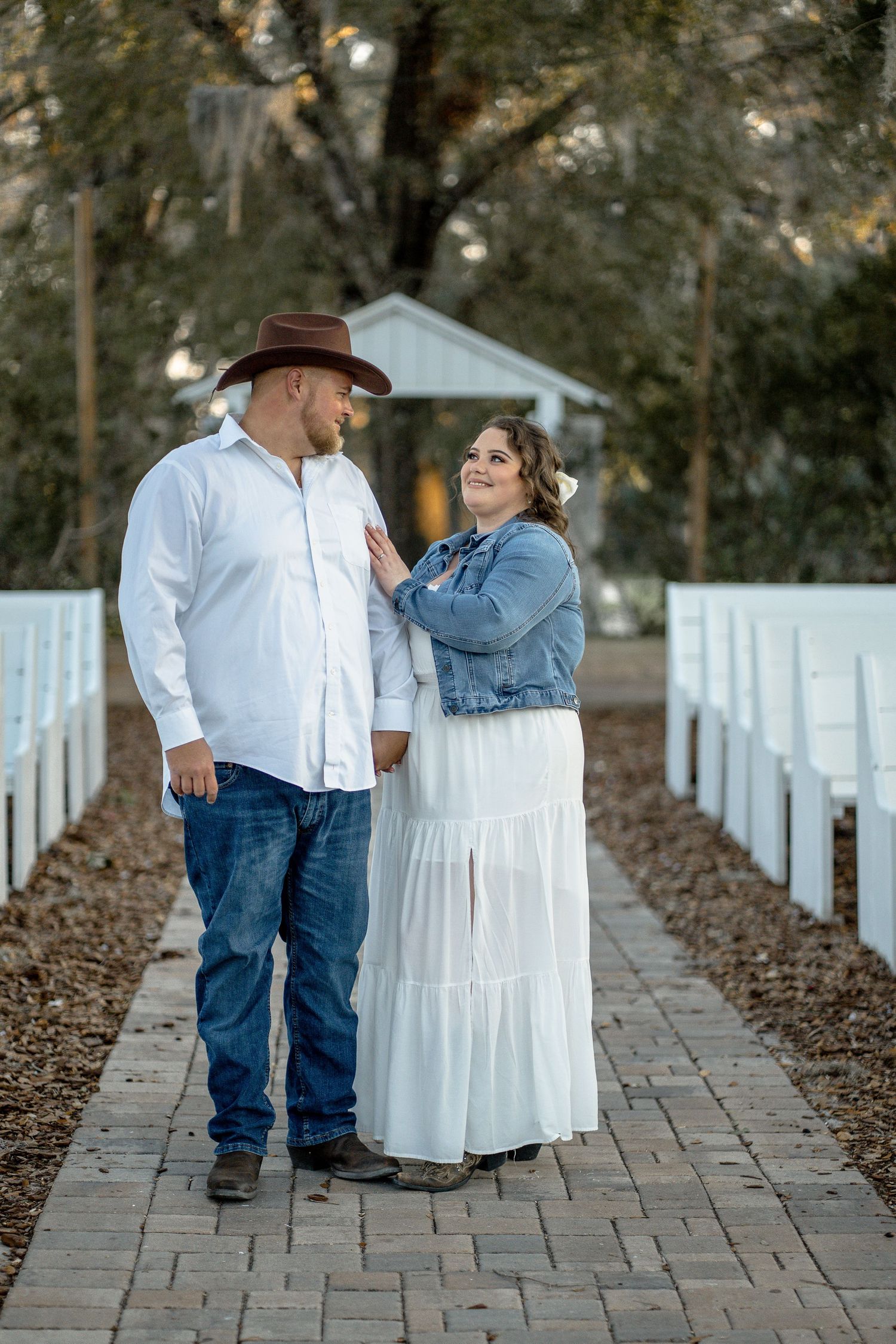 A couple poses together on a brick pathway surrounded by white fencing.
