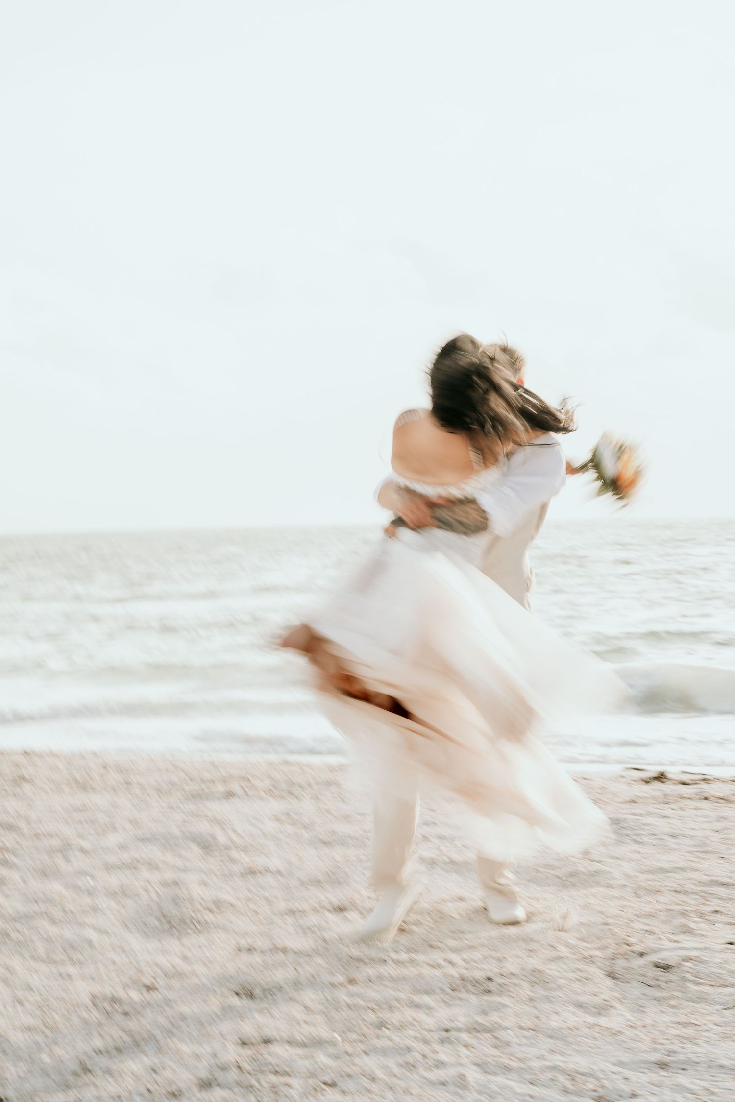 Ethereal photo of a twirling figure in white dress on a beach.