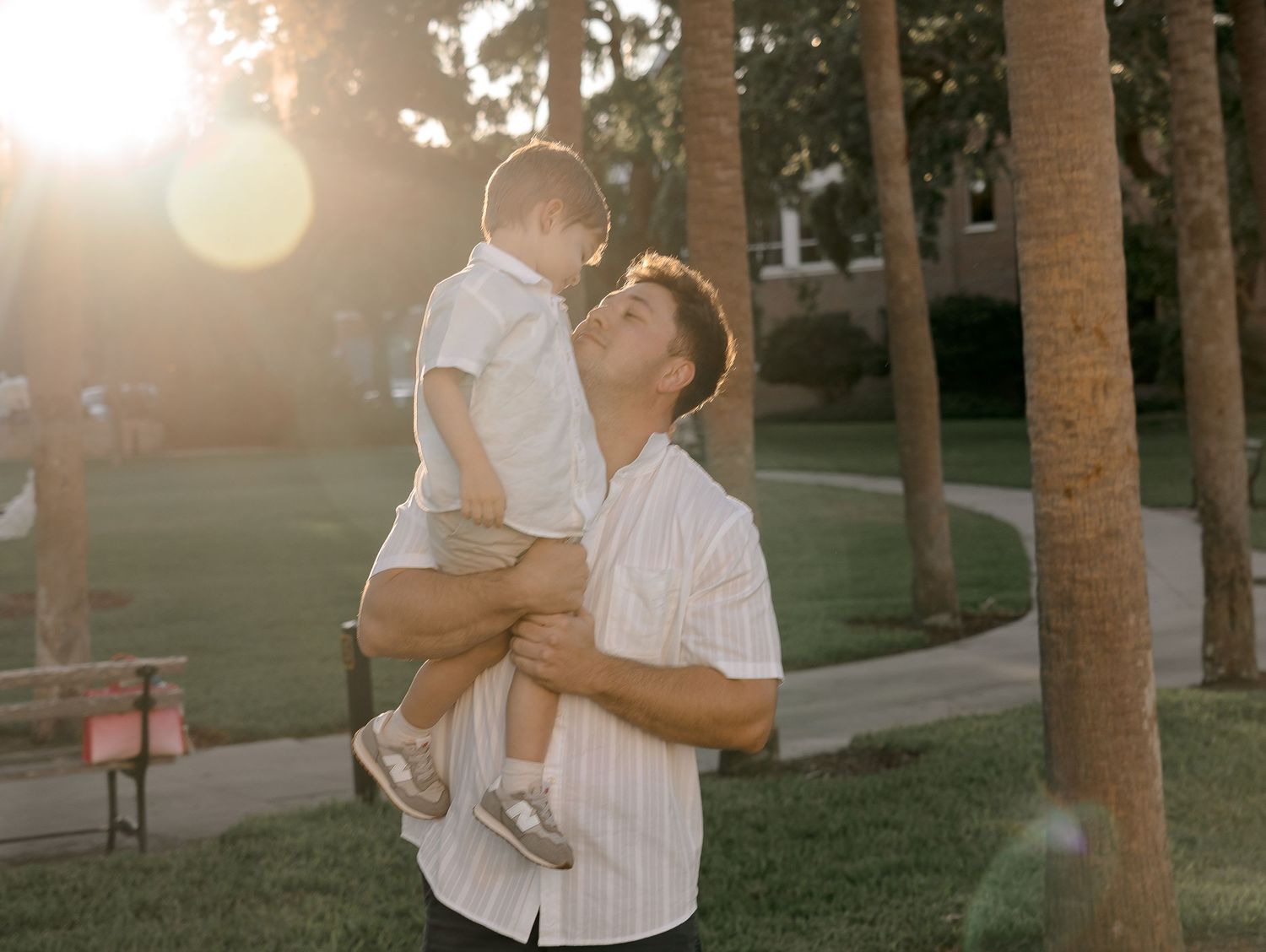 A couple shares tender moments with their newborn baby in a sunlit outdoor setting with palm trees.