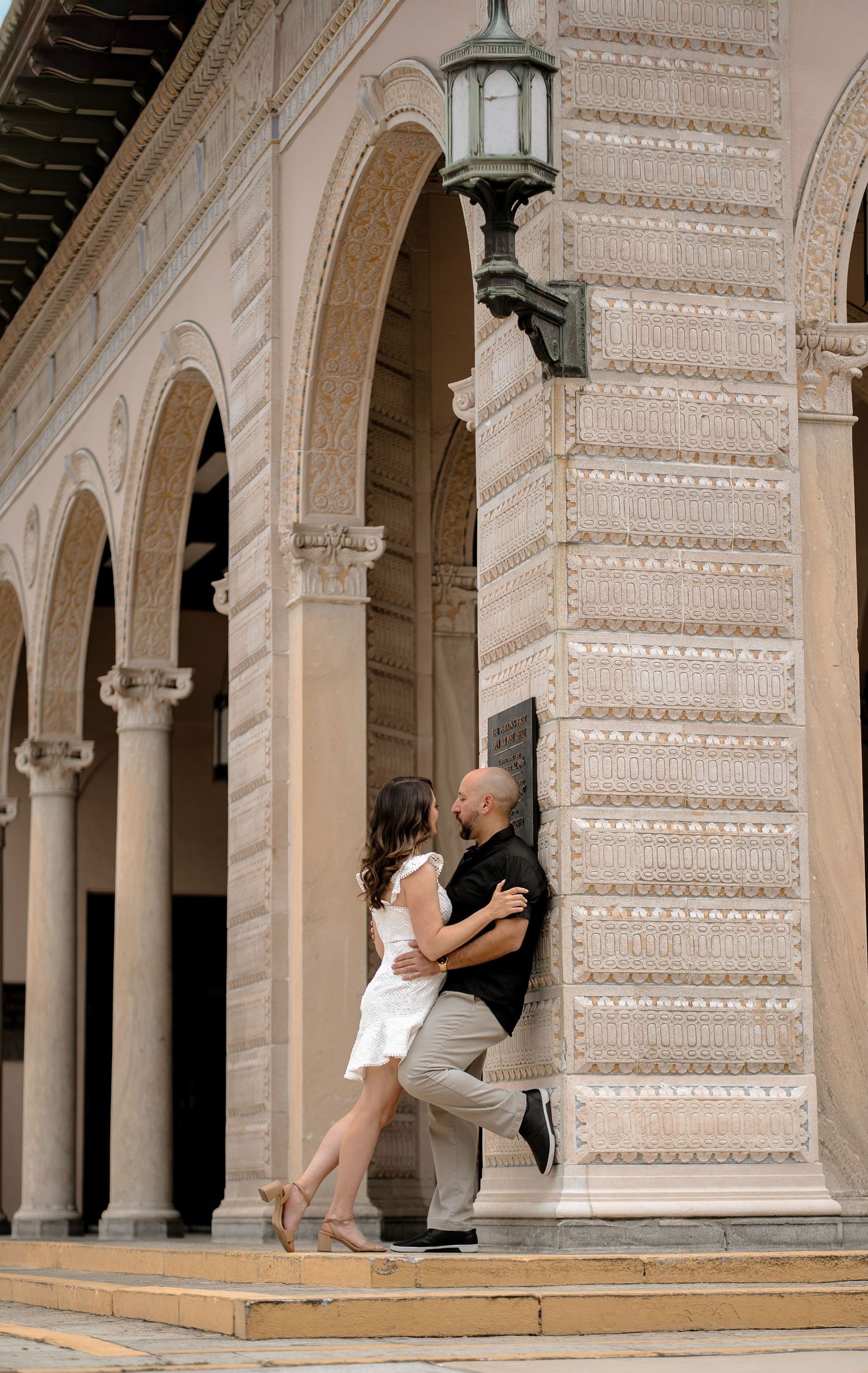 Couple posing playfully against classical architecture with arches and columns.