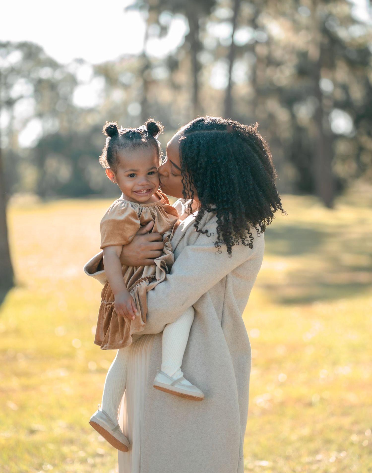 Tender moment captured in golden sunlit field wearing neutral tones.