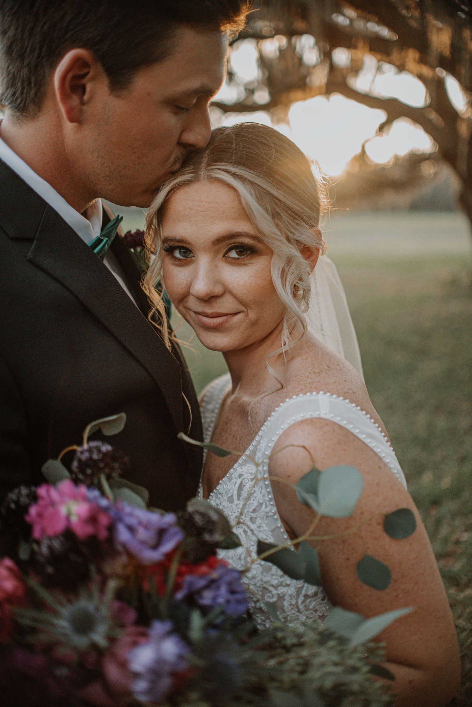 A romantic wedding portrait captures a tender moment between newlyweds at sunset.