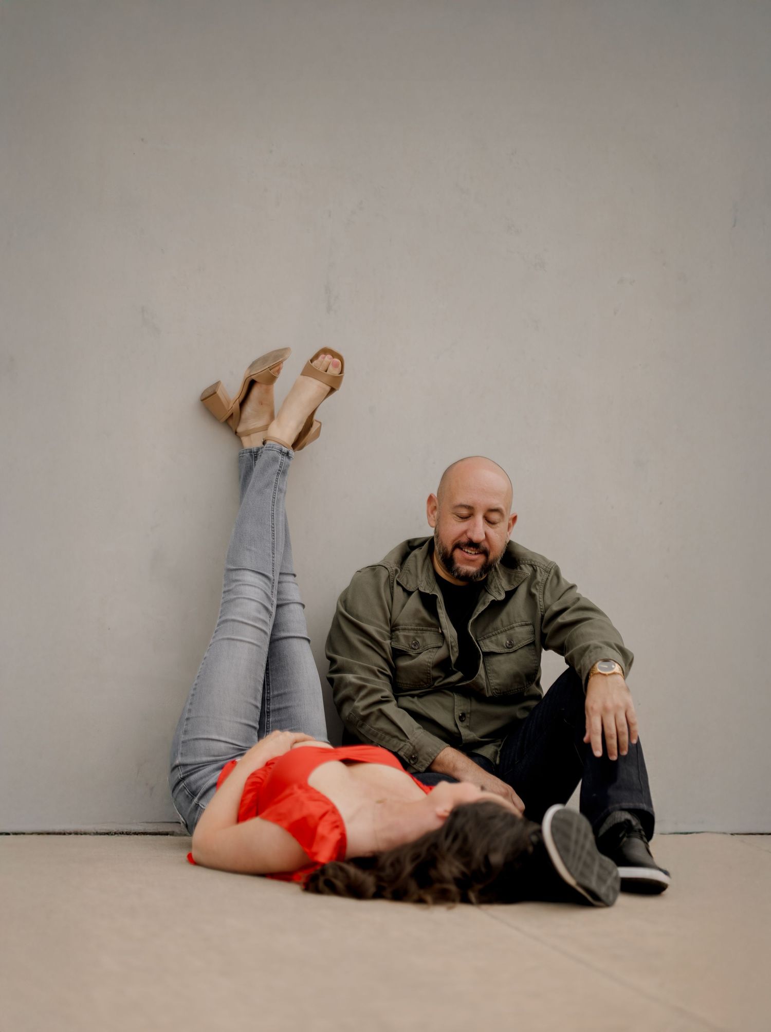 A playful couple poses together on a light gray studio floor in casual clothing.