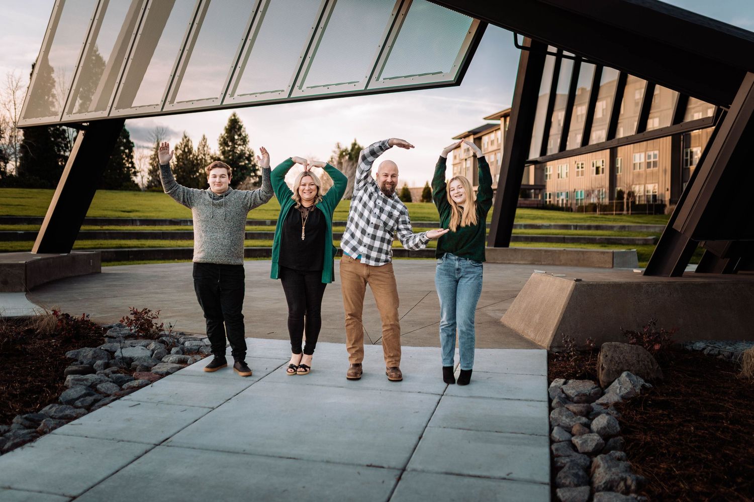 Four people raise their arms joyfully outside a modern glass building on a sunny day.