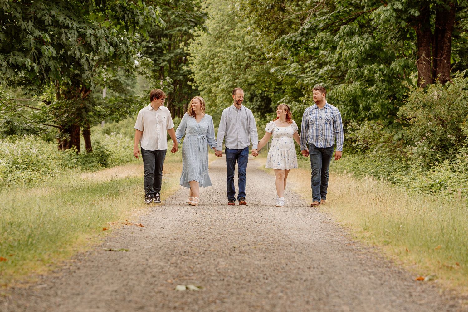 Family of five walking together on a scenic tree-lined path, dressed in coordinated casual outfits for a outdoor portrait session.