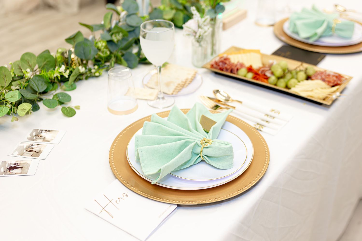 Elegant wedding reception place setting with mint green napkin, gold charger plate, and eucalyptus garland.