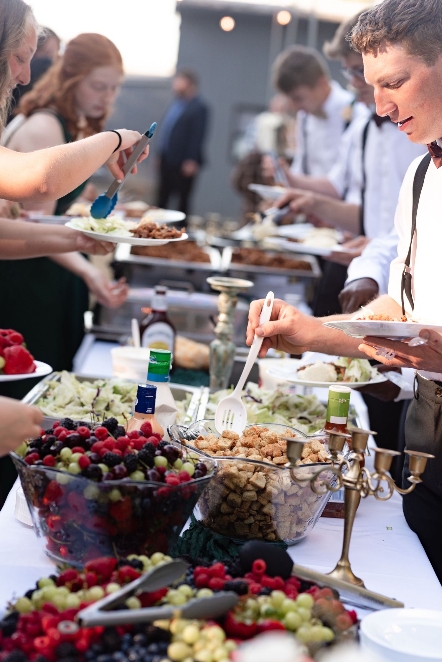 Guests serving themselves at an outdoor wedding buffet with fresh fruit and assorted dishes.