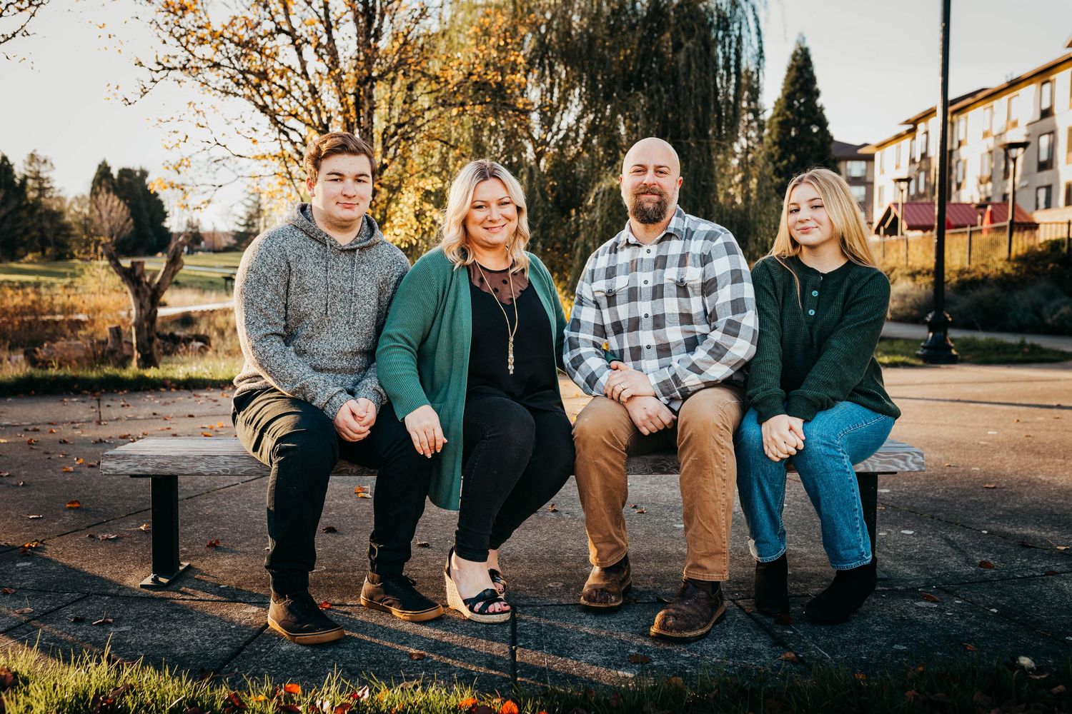 Family of four smiling together on a bench in a sunny autumn park with warm golden light.