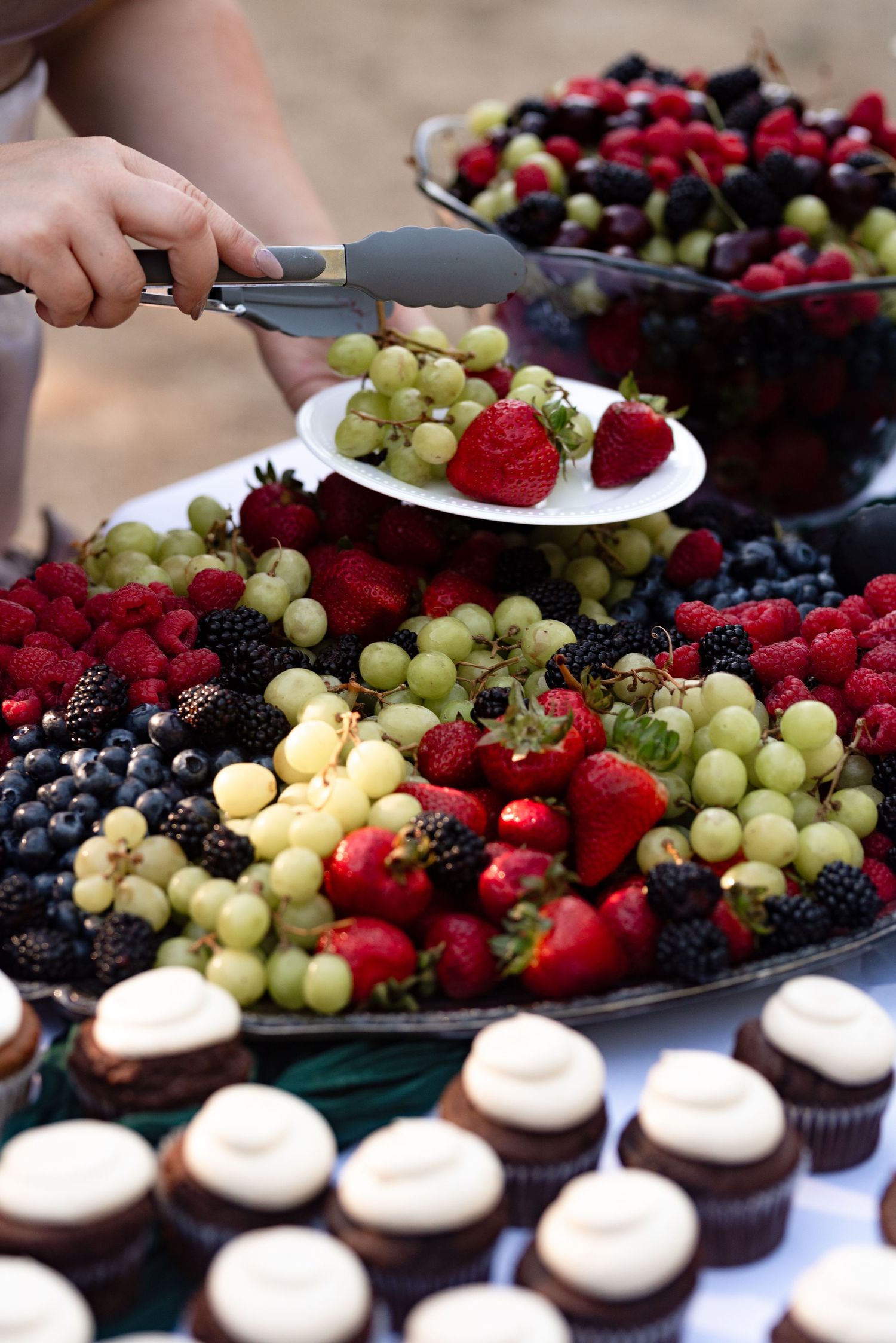 Beautiful wedding fruit display with grapes, strawberries, and berries beside chocolate cupcakes.