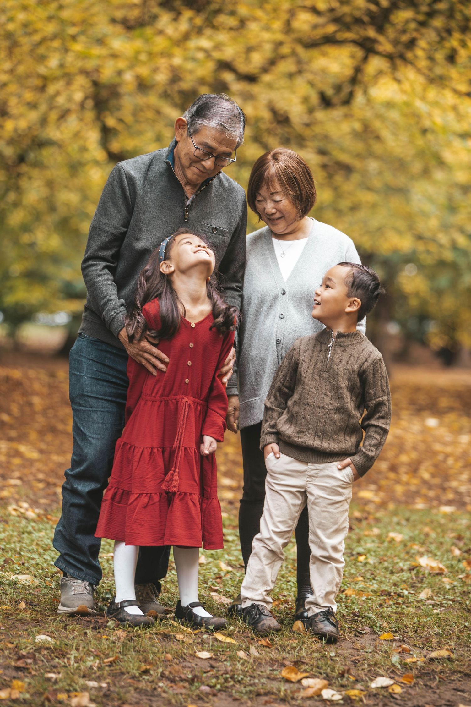Grandparents laughing and embracing two grandchildren in a colorful autumn park setting.
