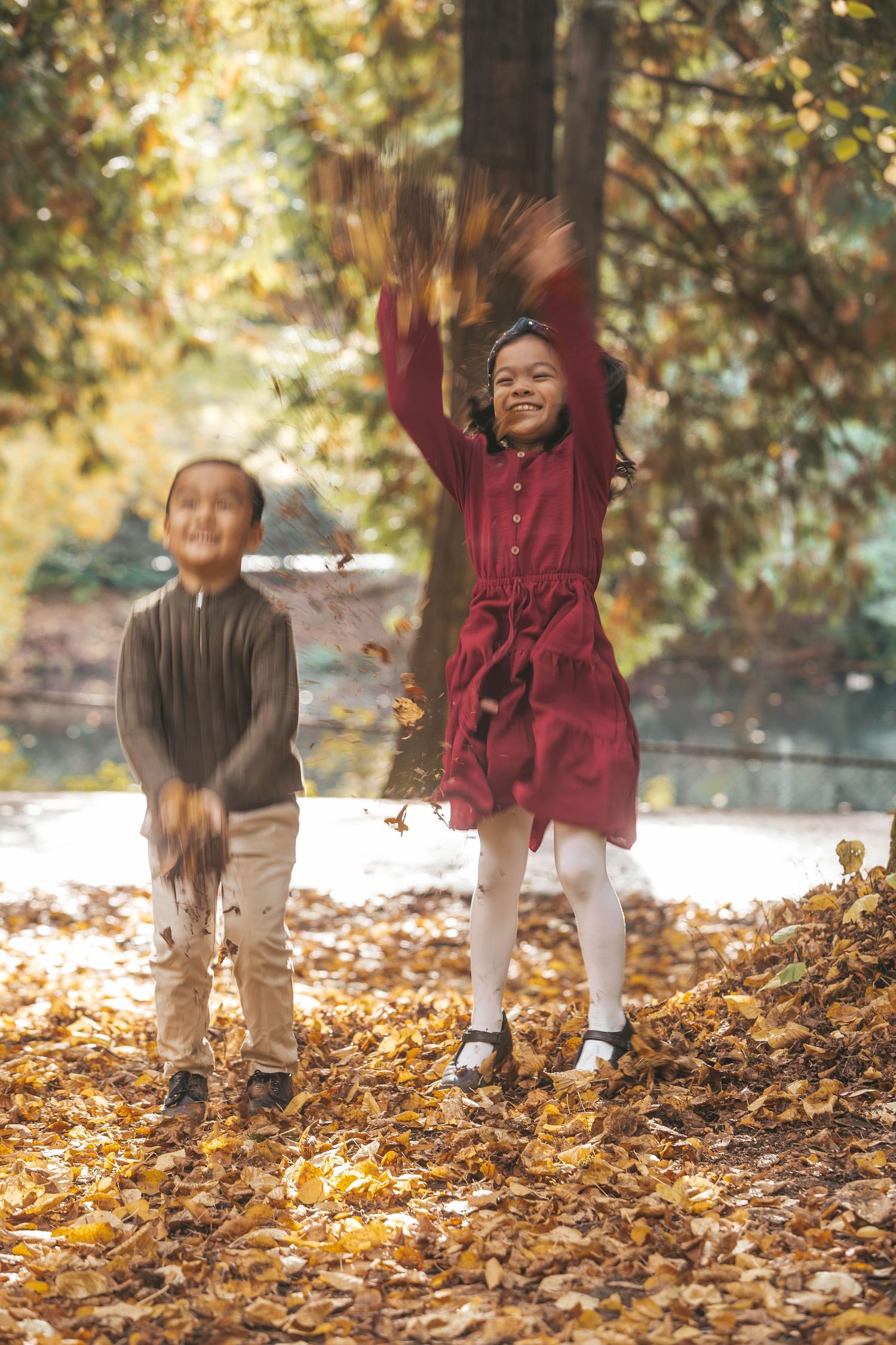 Two children joyfully tossing autumn leaves in a colorful fall park setting.
