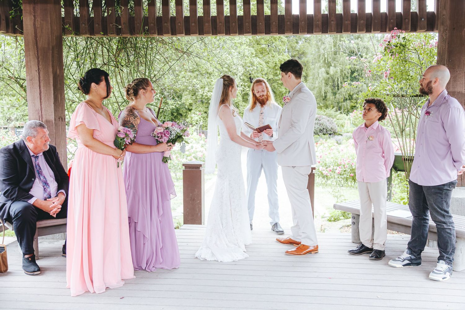 Small intimate wedding ceremony in a wooden gazebo with bridesmaids in pink dresses.