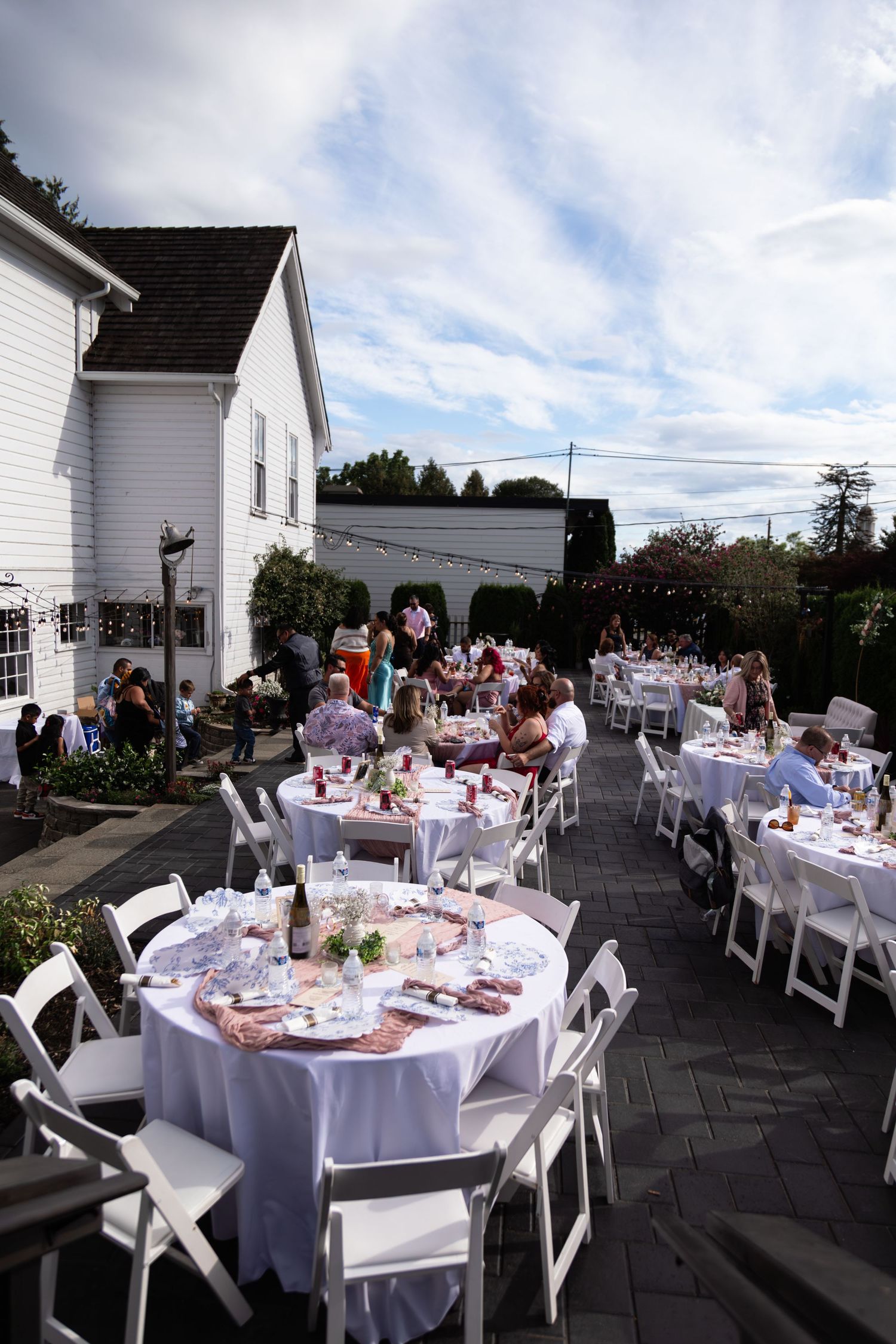 Outdoor wedding reception with white round tables and chairs at a charming white venue.