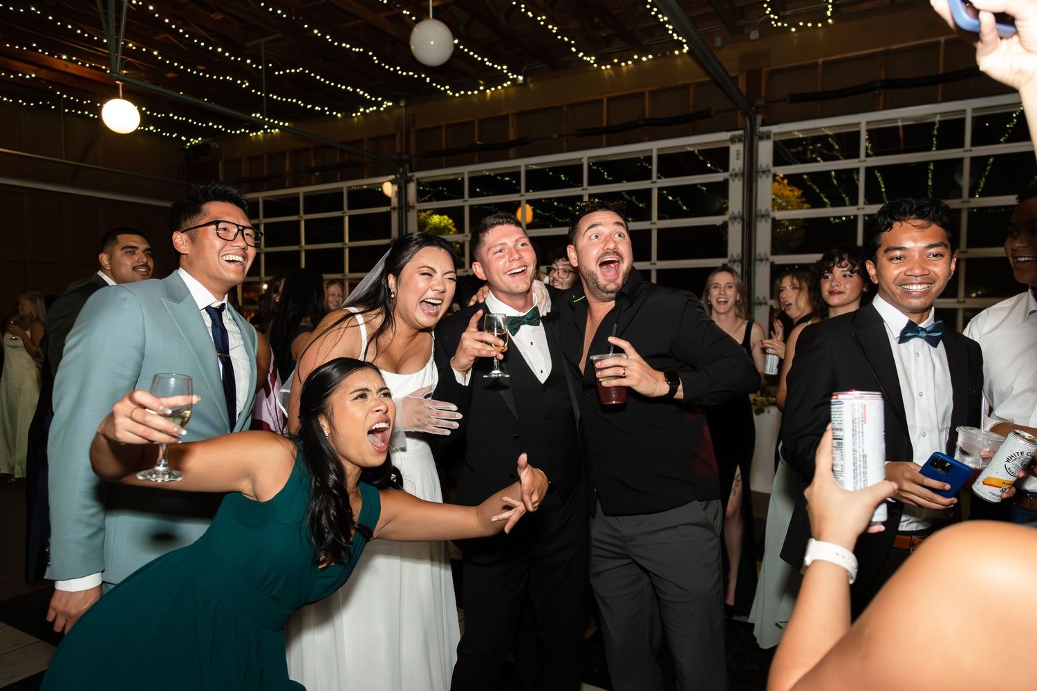 Bride and groom celebrating with guests on the dance floor at a lively wedding reception.