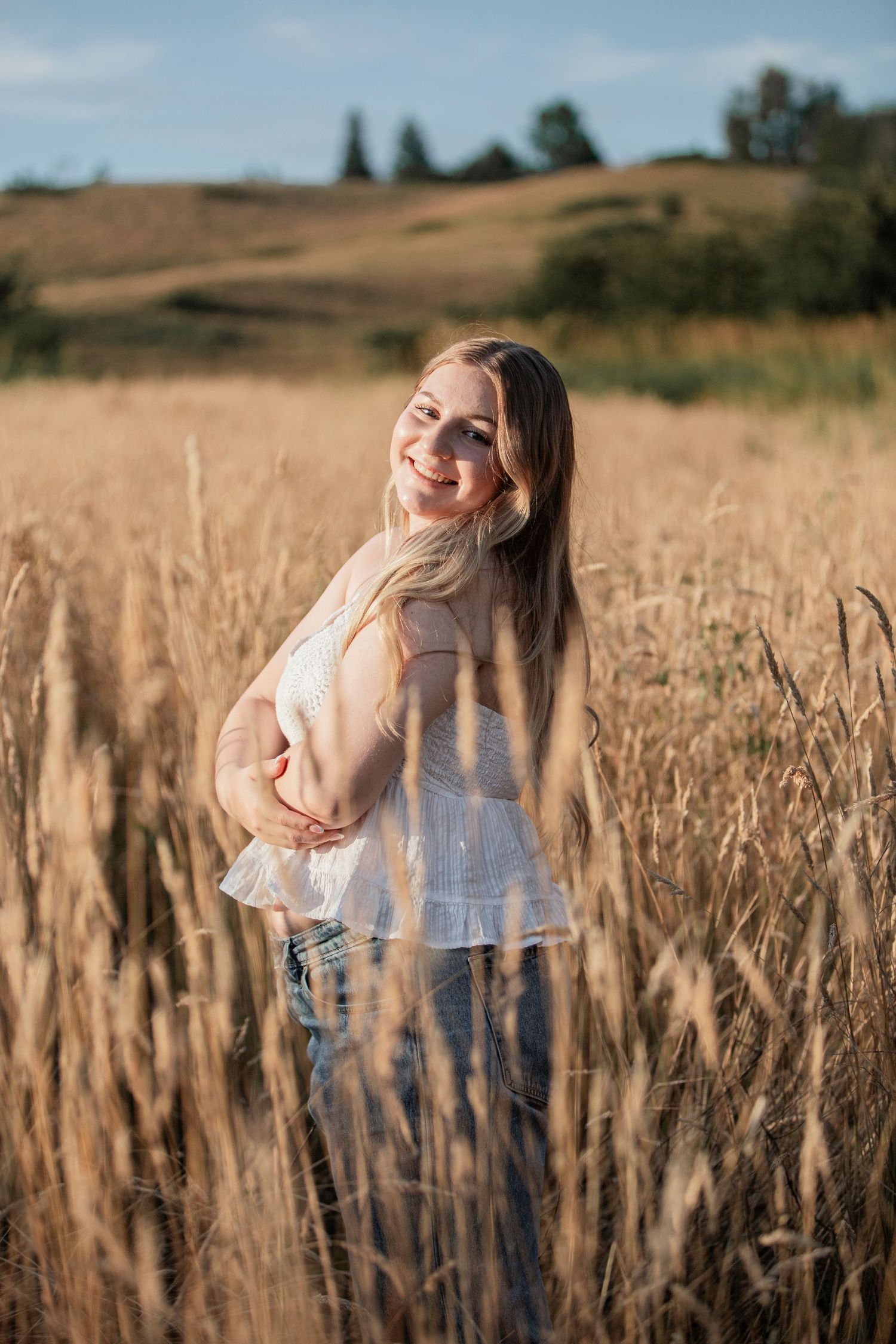 Smiling young woman in white blouse standing in golden wheat field on sunny day.