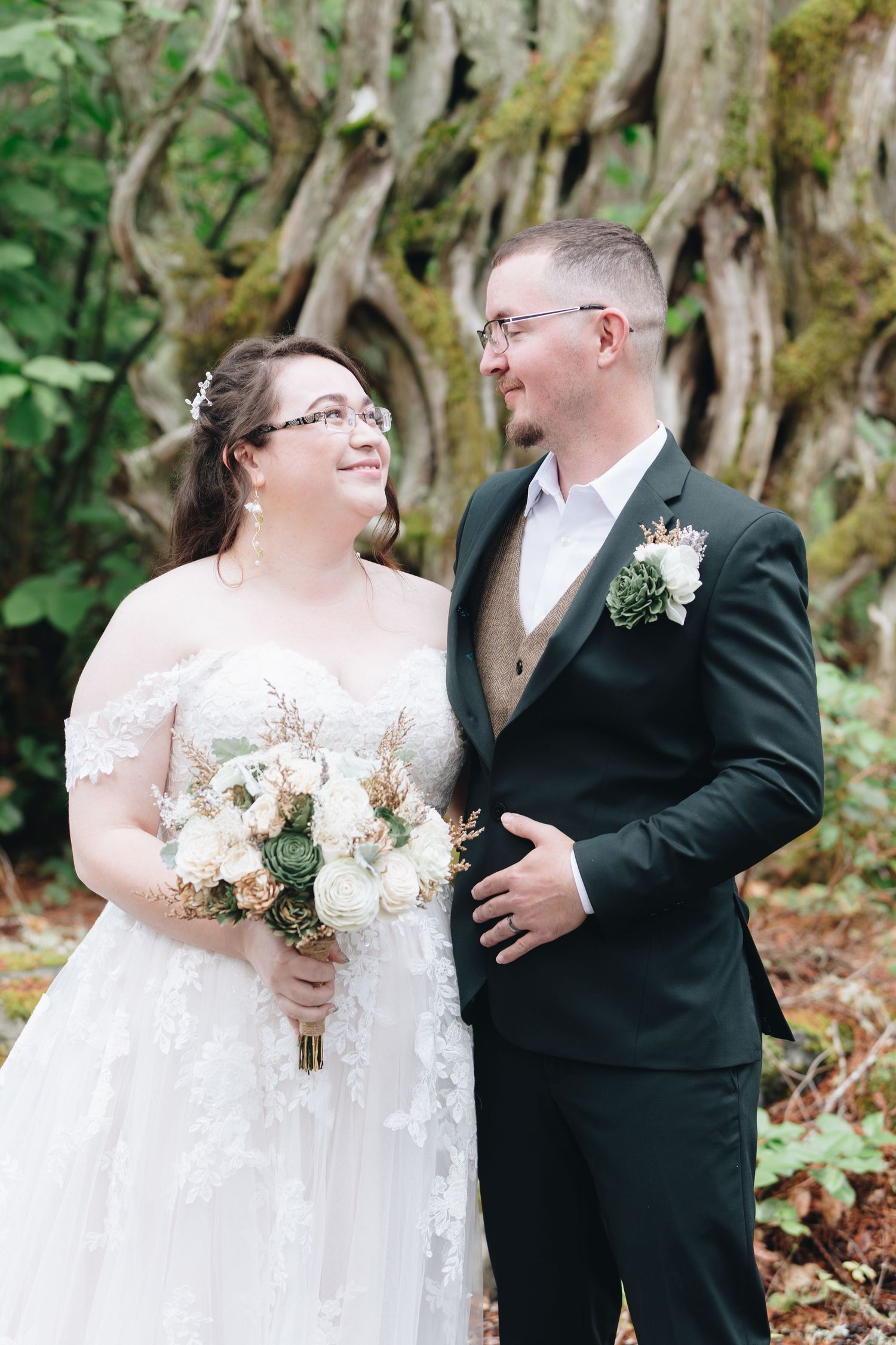 Bride and groom sharing a romantic moment in front of moss-covered tree in forest wedding.