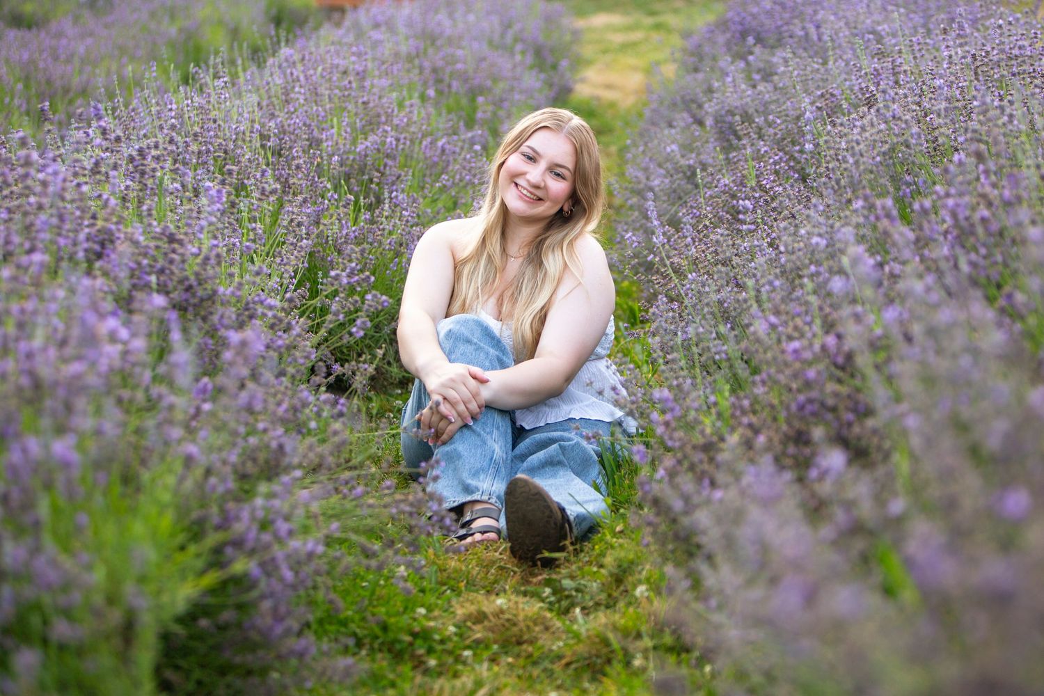 Smiling blonde girl crouching in rows of purple lavender flowers in a garden field.