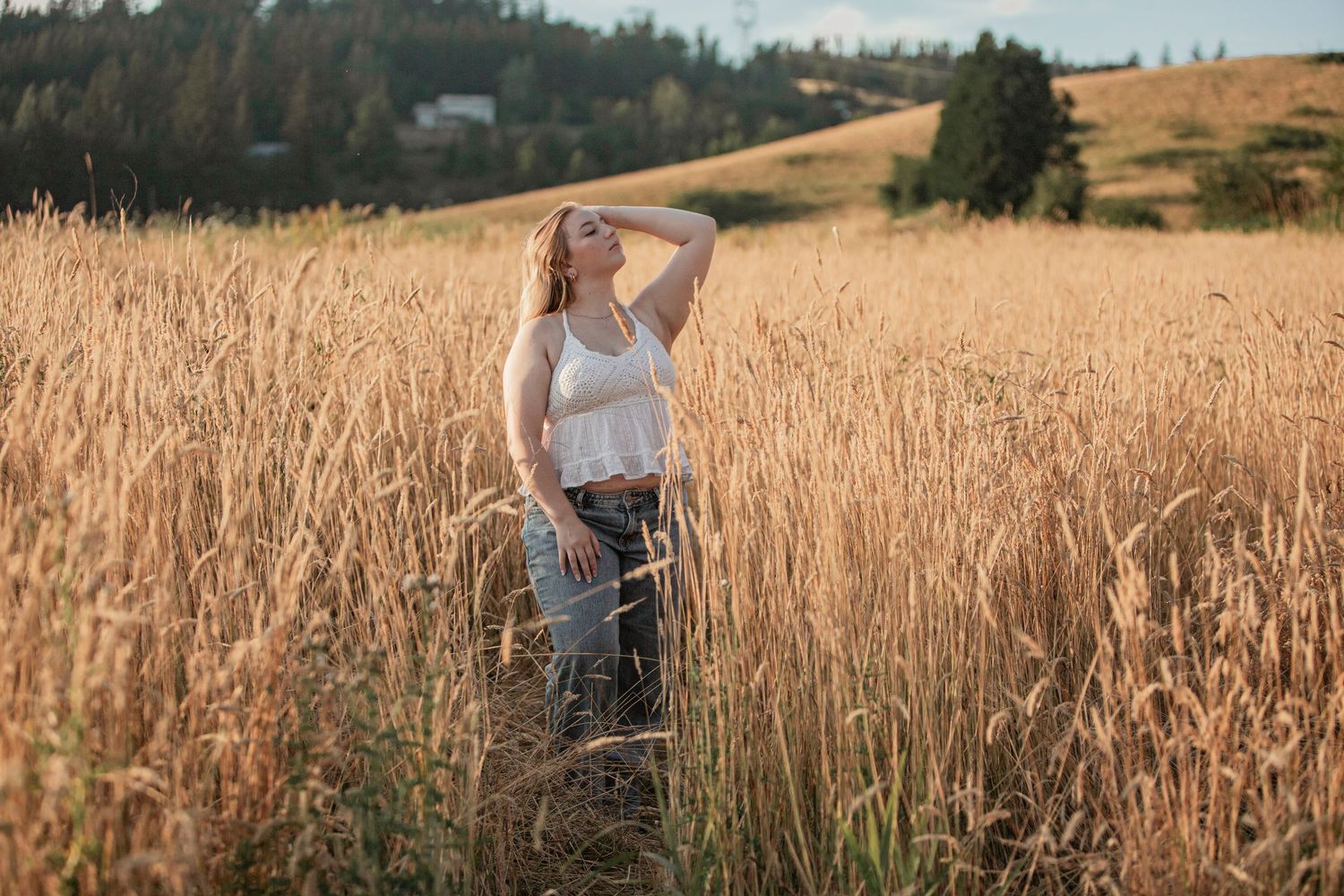 Young woman in white top posing in tall golden wheat field on a sunny day.