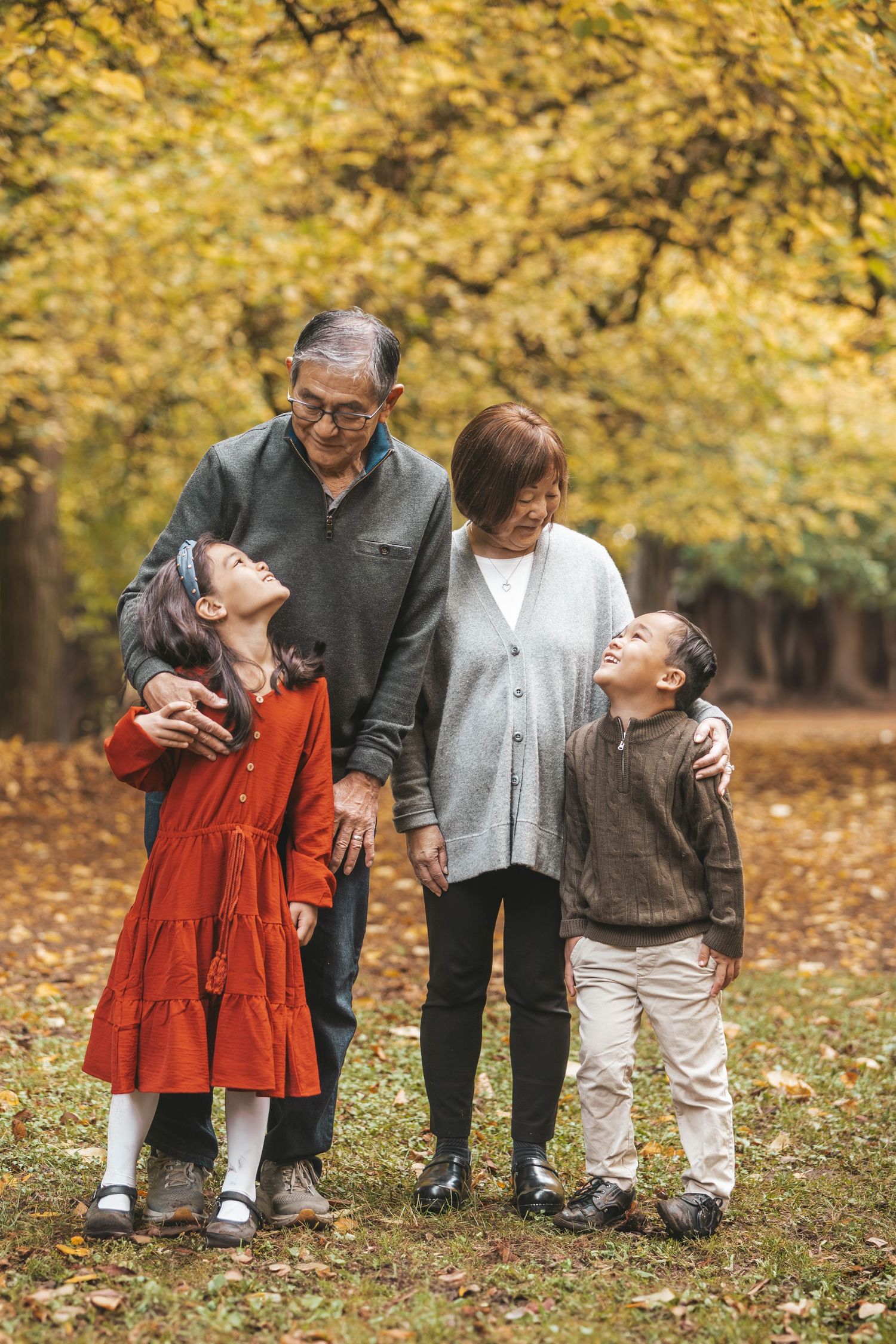 Grandparents walking with grandchildren in autumn park, smiling and embracing among golden fall foliage.