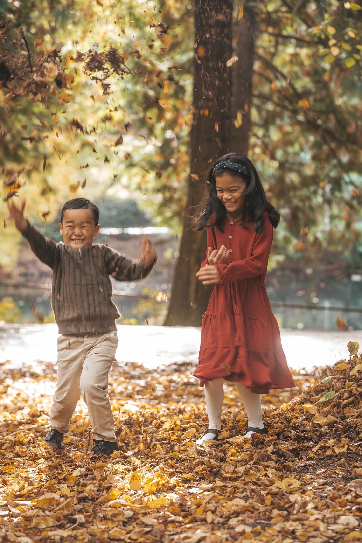 Two children laughing and playing in golden autumn leaves in a sunny park.