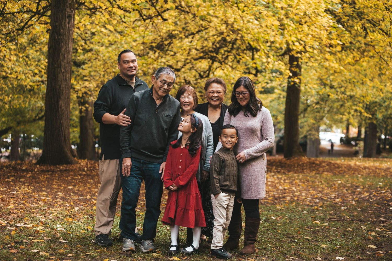 Multi-generational Asian family posing together under golden autumn trees in a park.