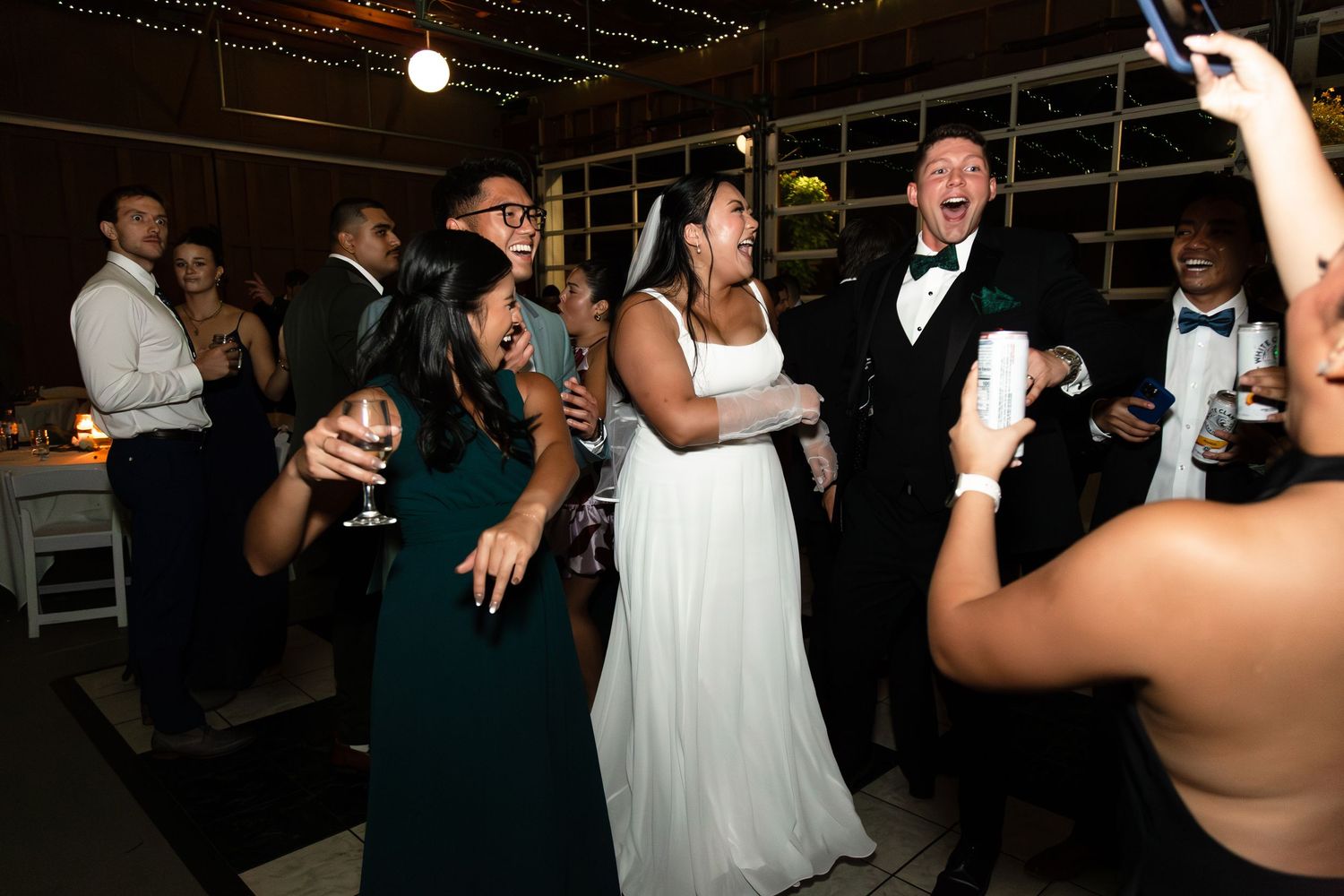 Bride and groom dancing joyfully with guests at a lively wedding reception celebration.