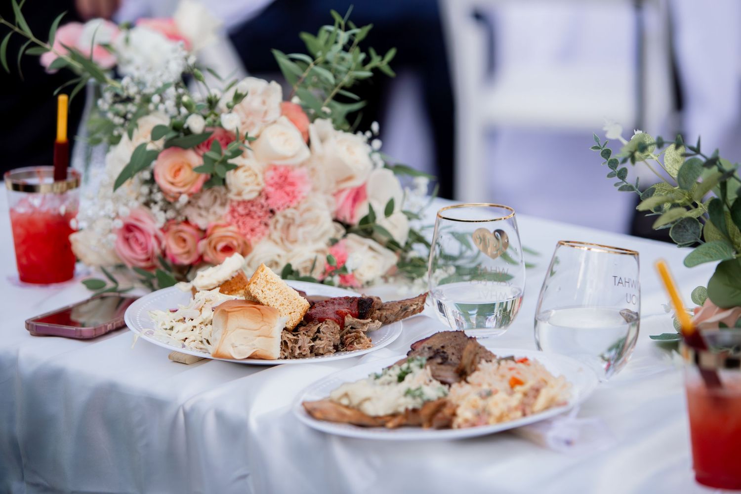 Wedding reception table with floral bouquet, food plates, and elegant glassware.