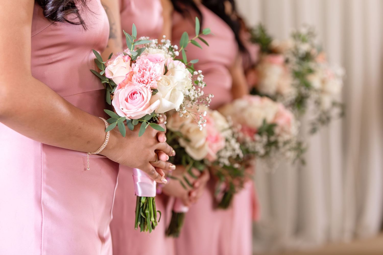 Bridesmaids in pink dresses holding bouquets of pink roses and white flowers at a wedding ceremony.