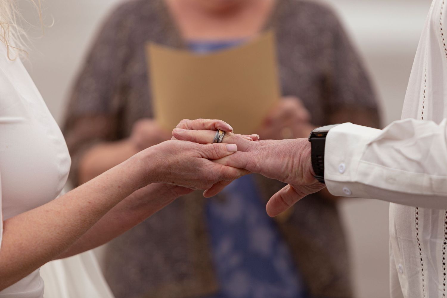 Close-up of wedding ring exchange ceremony with officiant holding book in background.