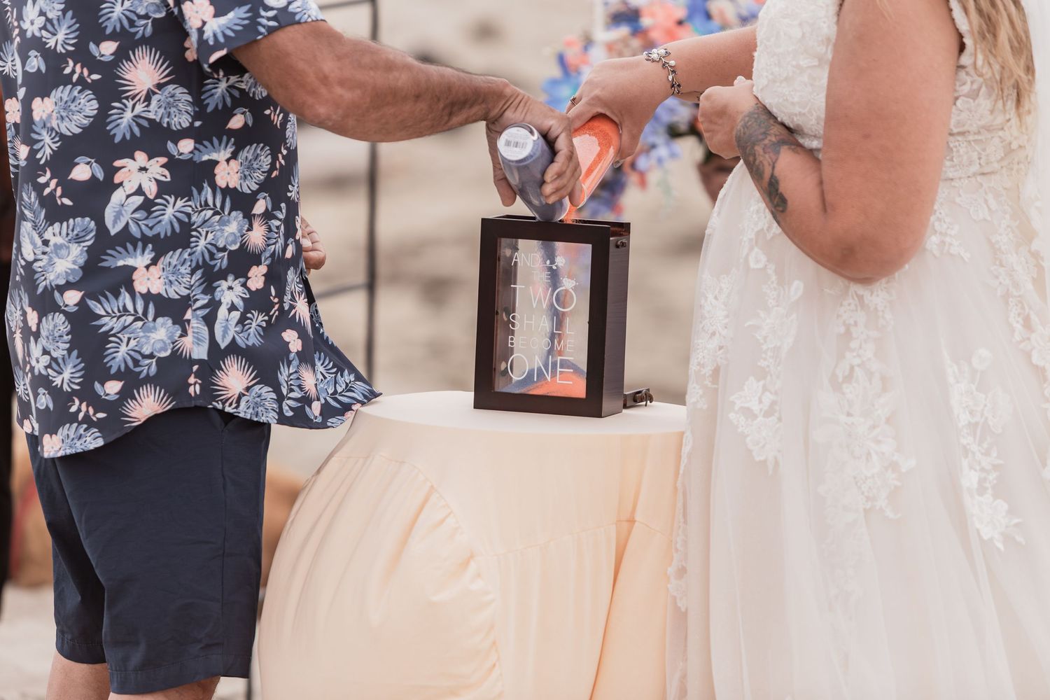 Officiant and bride performing sand ceremony ritual in decorative frame at beach wedding.