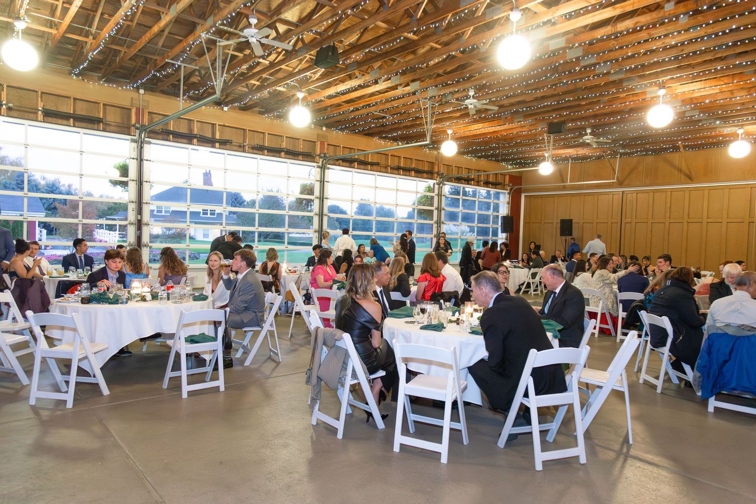Elegant indoor wedding reception with white chairs and round tables in a rustic venue.