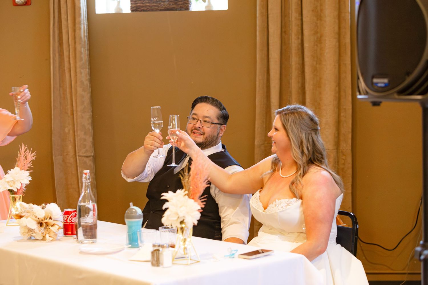 Newlywed couple toasting with champagne glasses at wedding reception sweetheart table.