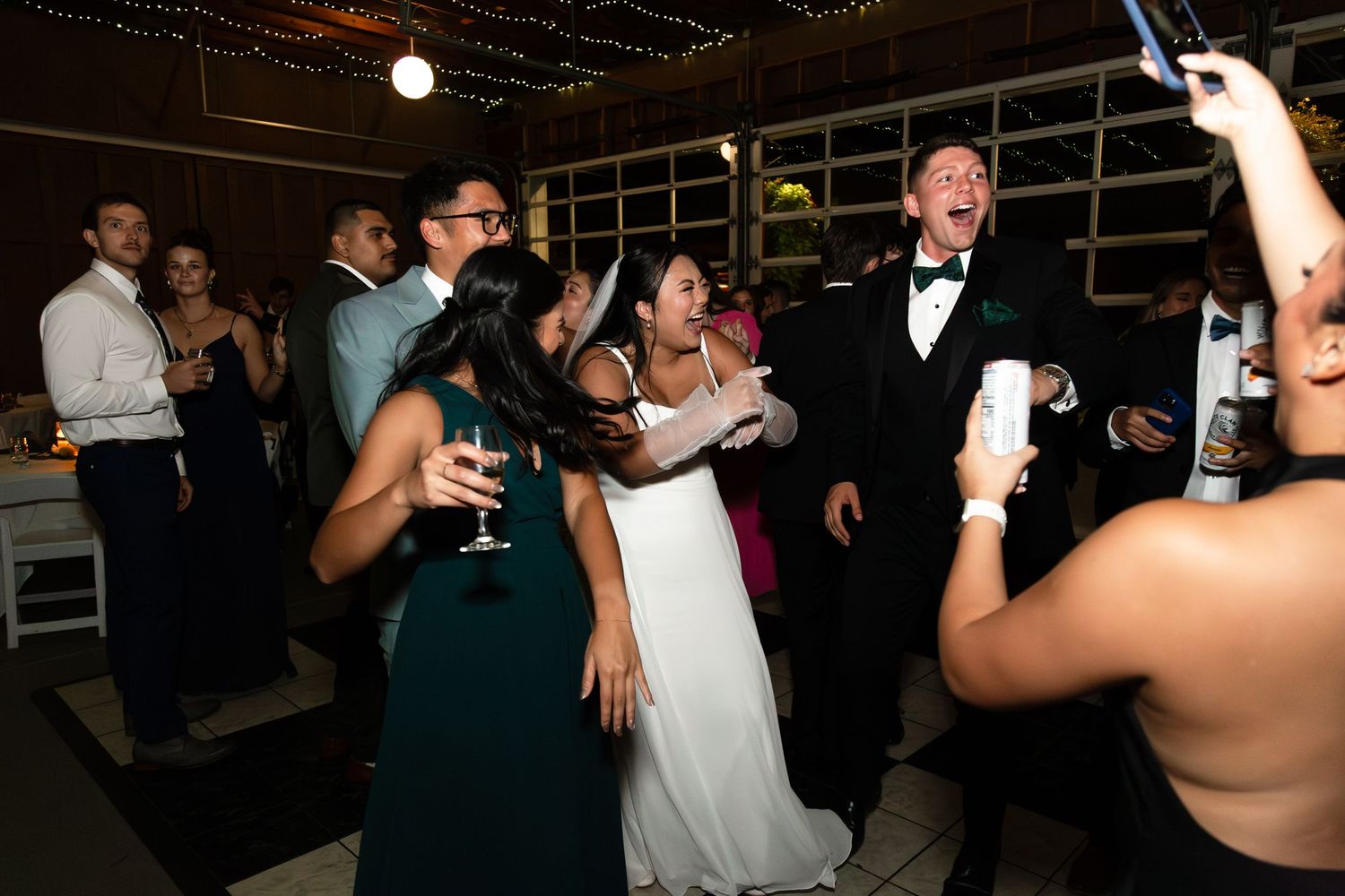 Bride and groom dancing joyfully with guests at a lively indoor wedding reception celebration.
