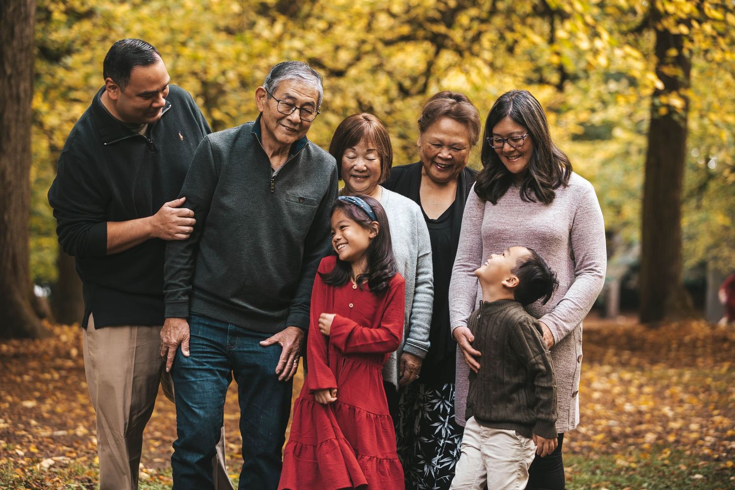 Multigenerational Asian family smiling together in autumn park with golden yellow trees.