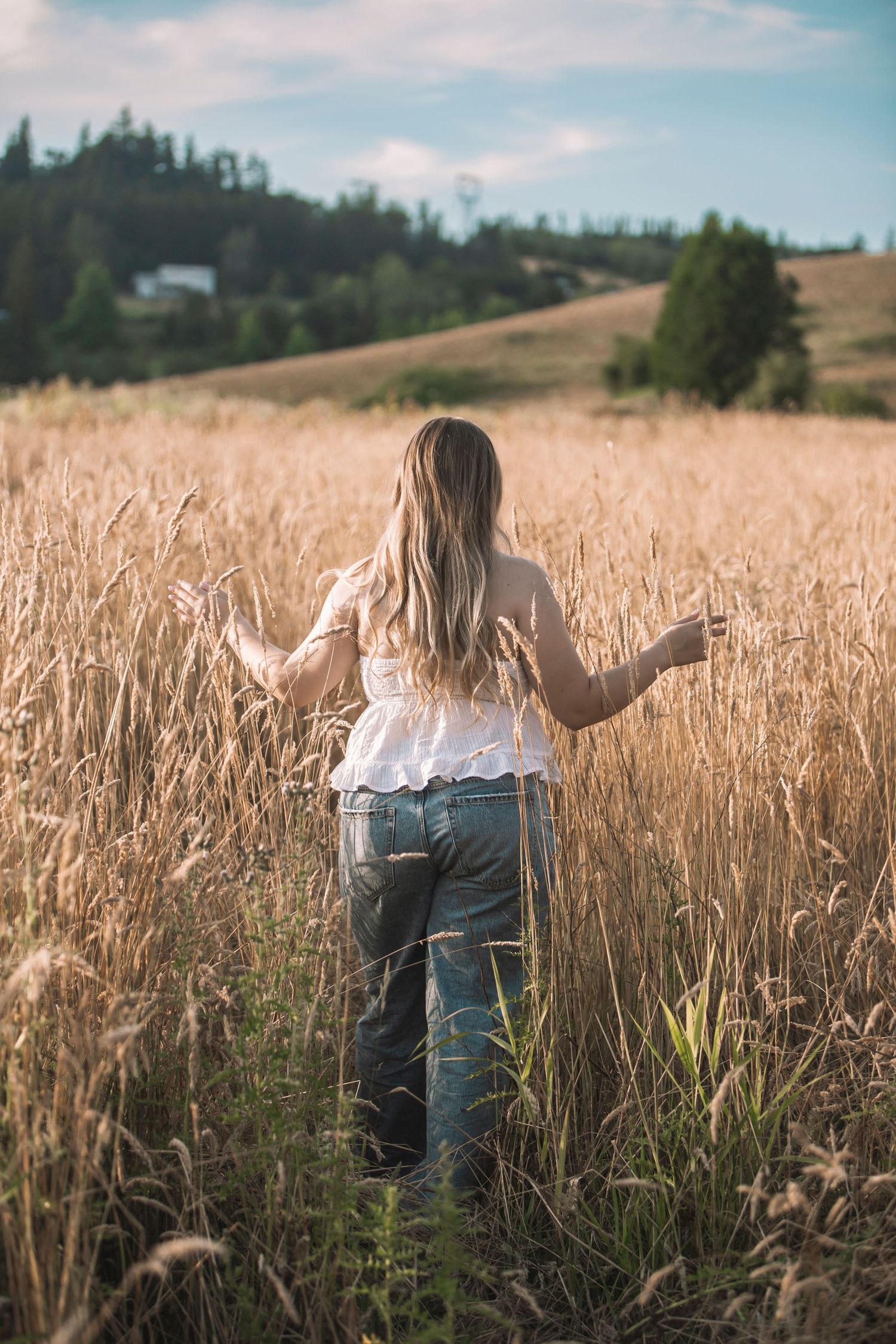Woman in white top and jeans walking through golden wheat field on sunny day.