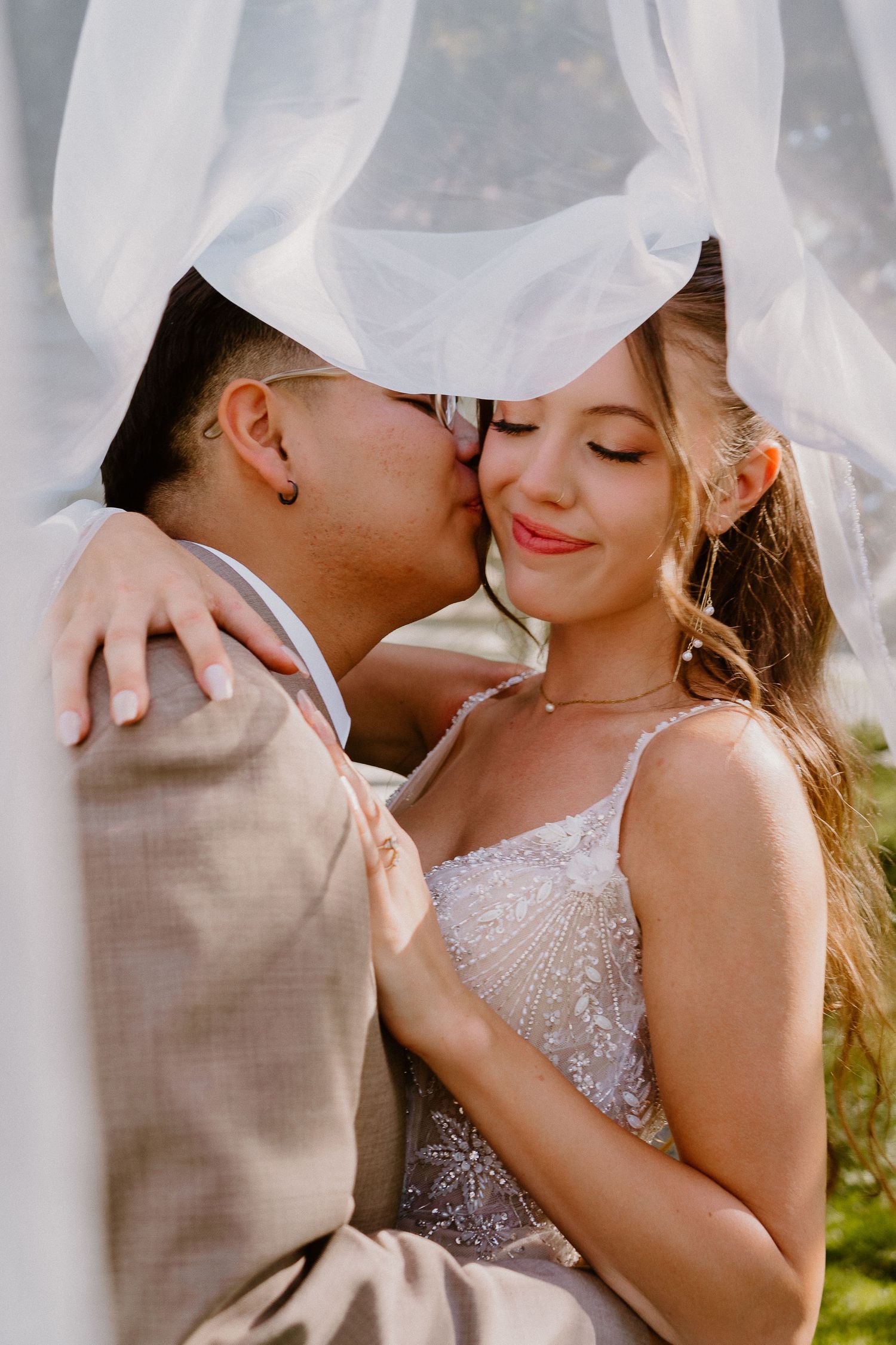 Bride and groom sharing intimate moment beneath veil during wedding portraits
