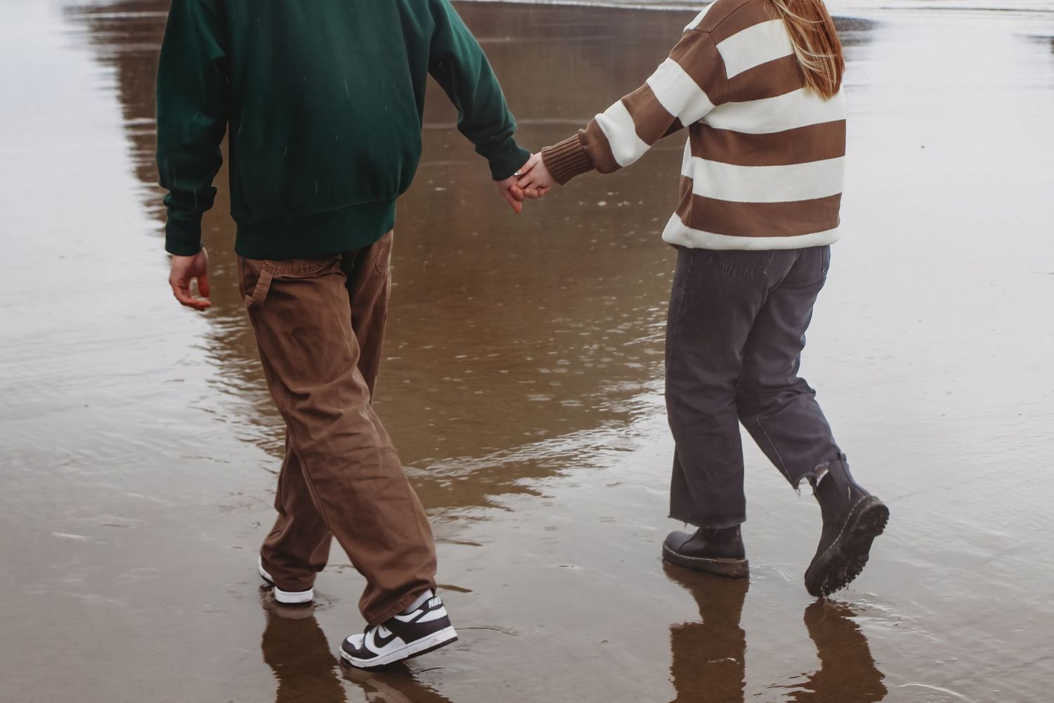 Couple holding hands while walking through shallow water during playful session at canon beach, oregon