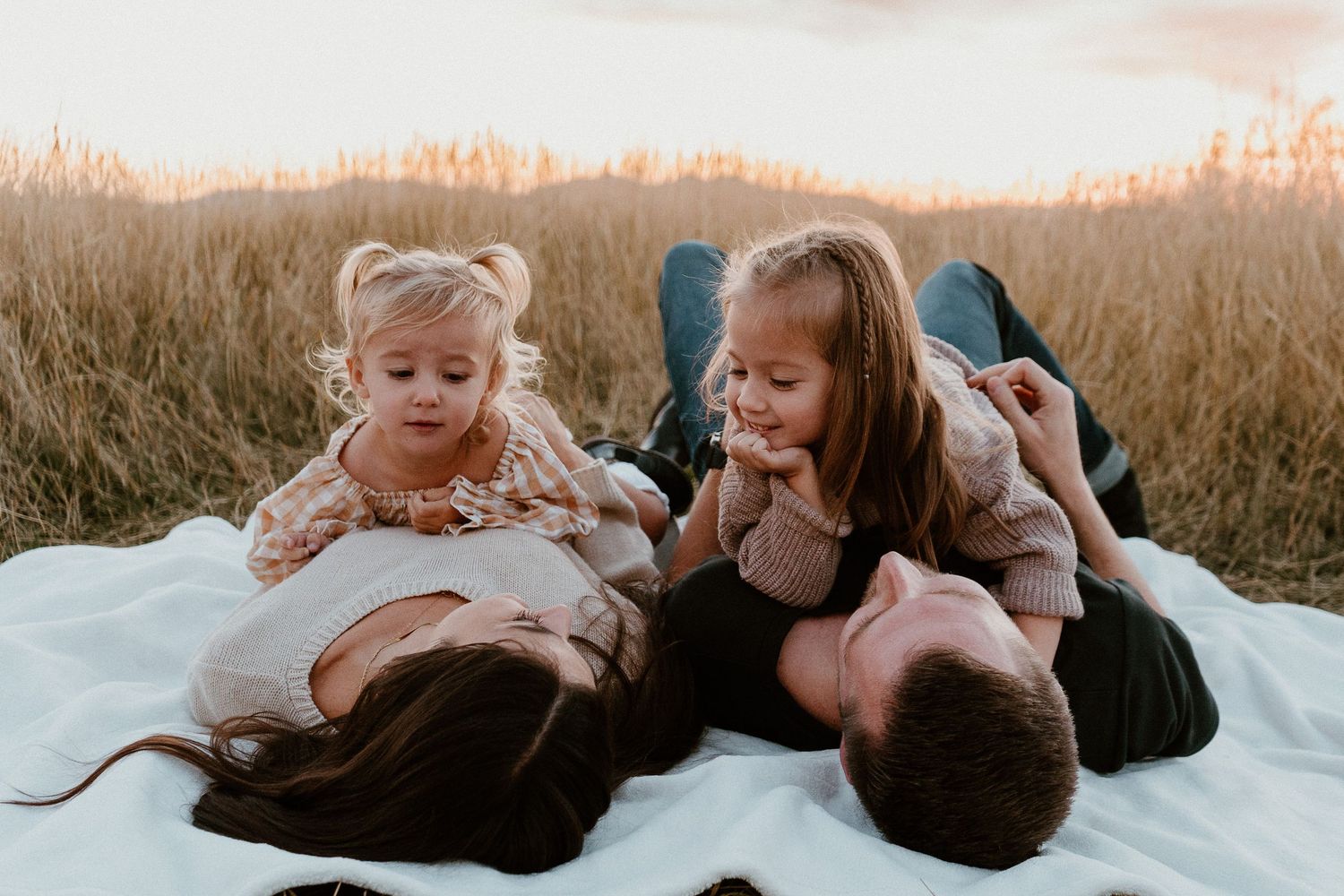 Parents relaxing with children on blanket during playful family sunset session