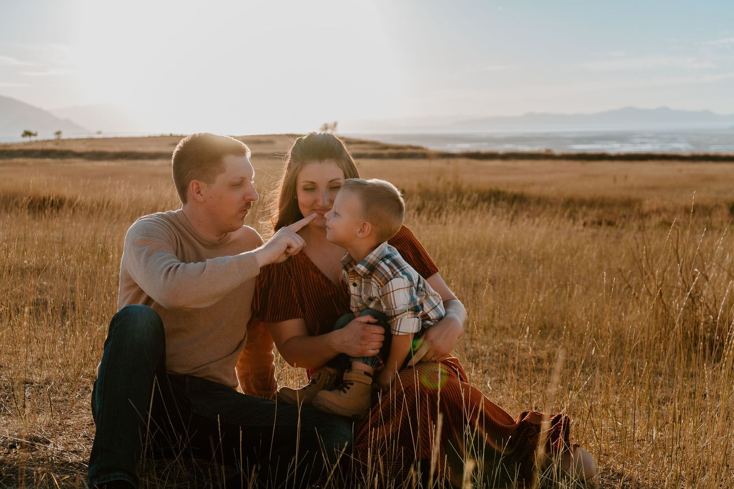 Family of three cuddling together in golden field during sunset family session