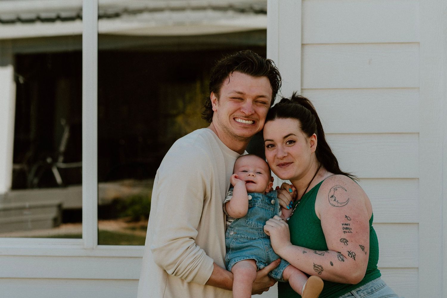 Young family portrait with parents holding baby outside home