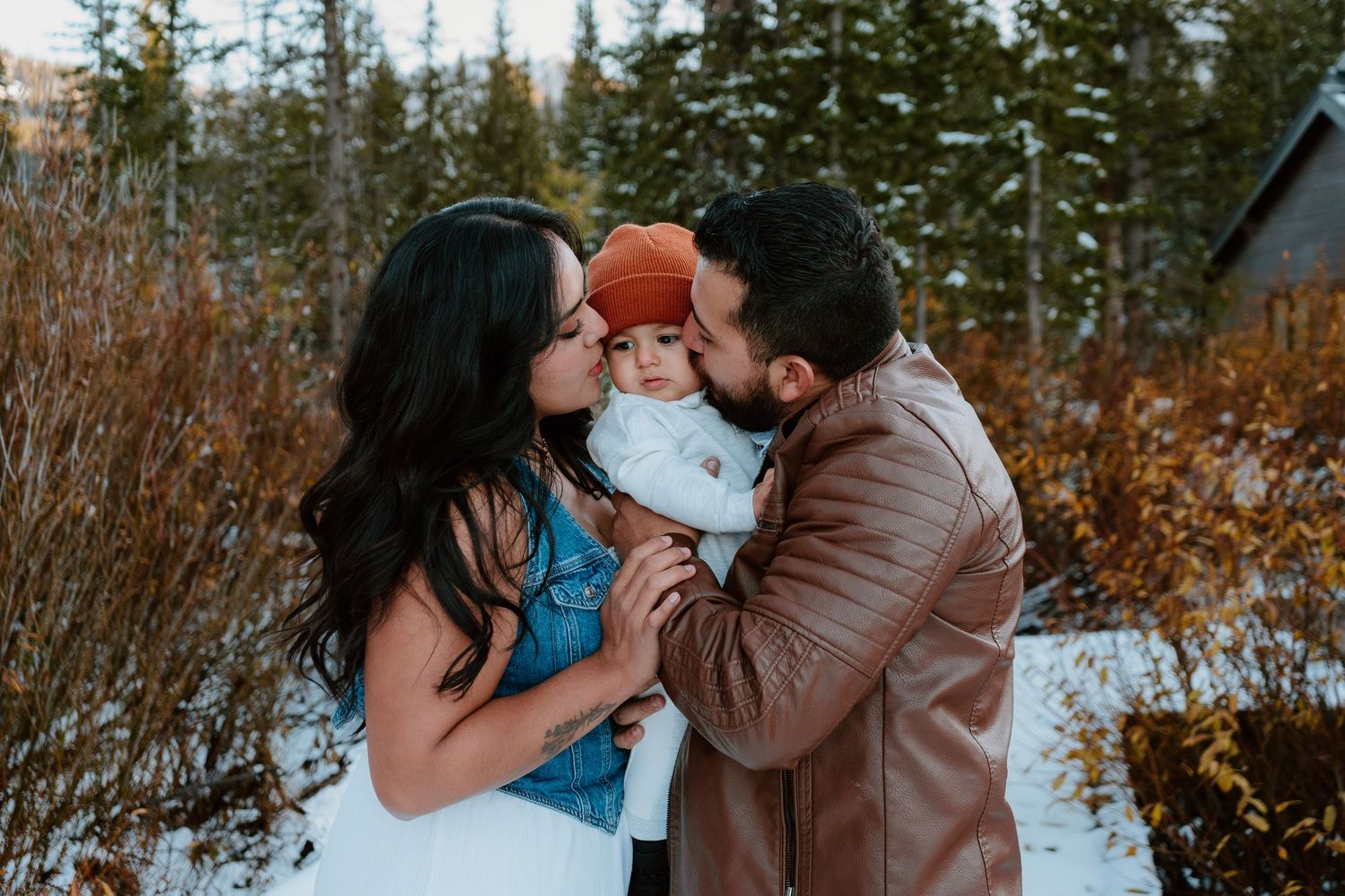 Parents kissing baby during cozy winter family session outdoors