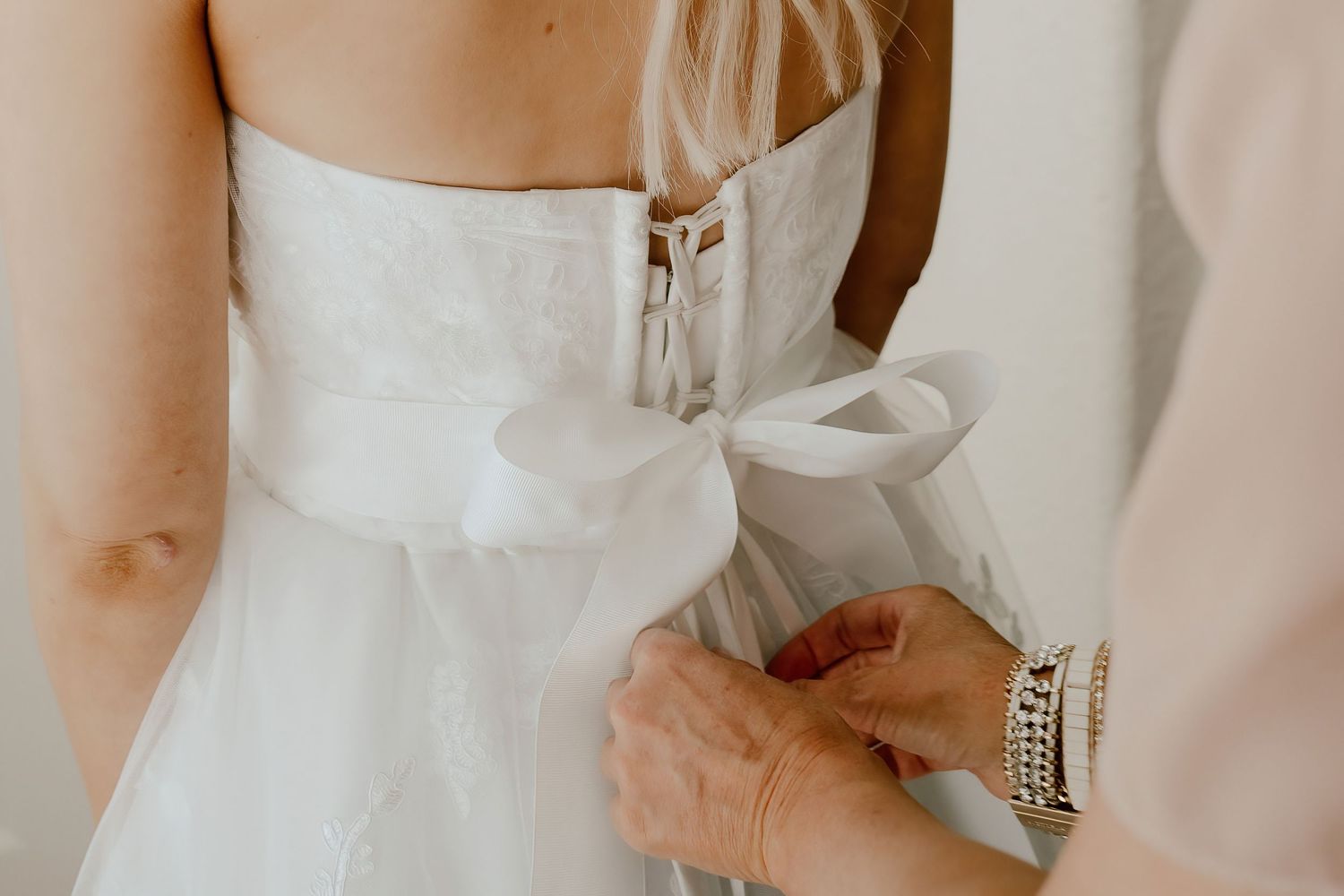 Wedding dress detail photo of bride getting ready with gown being tied