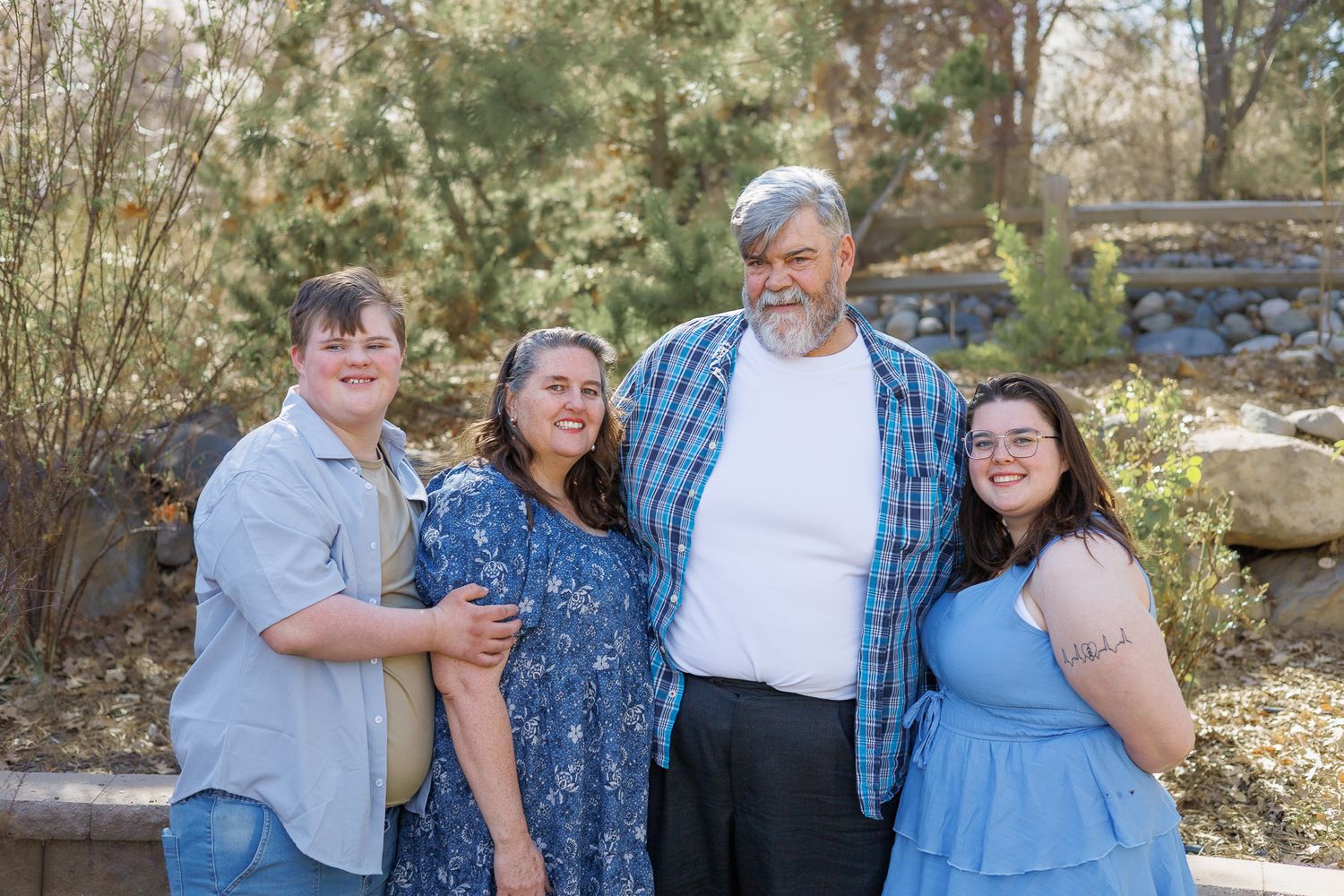 Family of four smiling together outdoors near a rocky landscape on a sunny day.