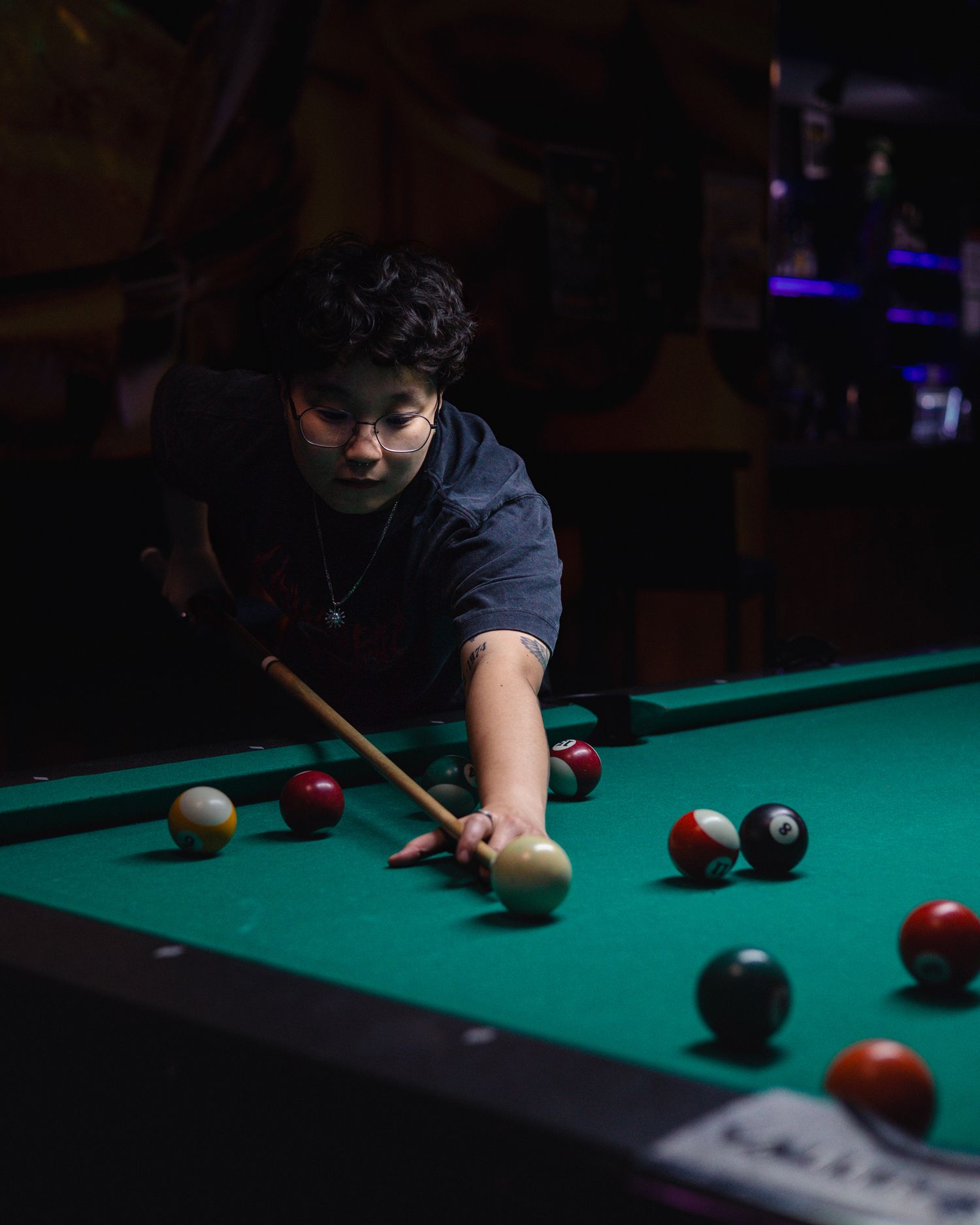 Young person leaning over a green billiard table lining up a pool shot with colorful balls on the felt.