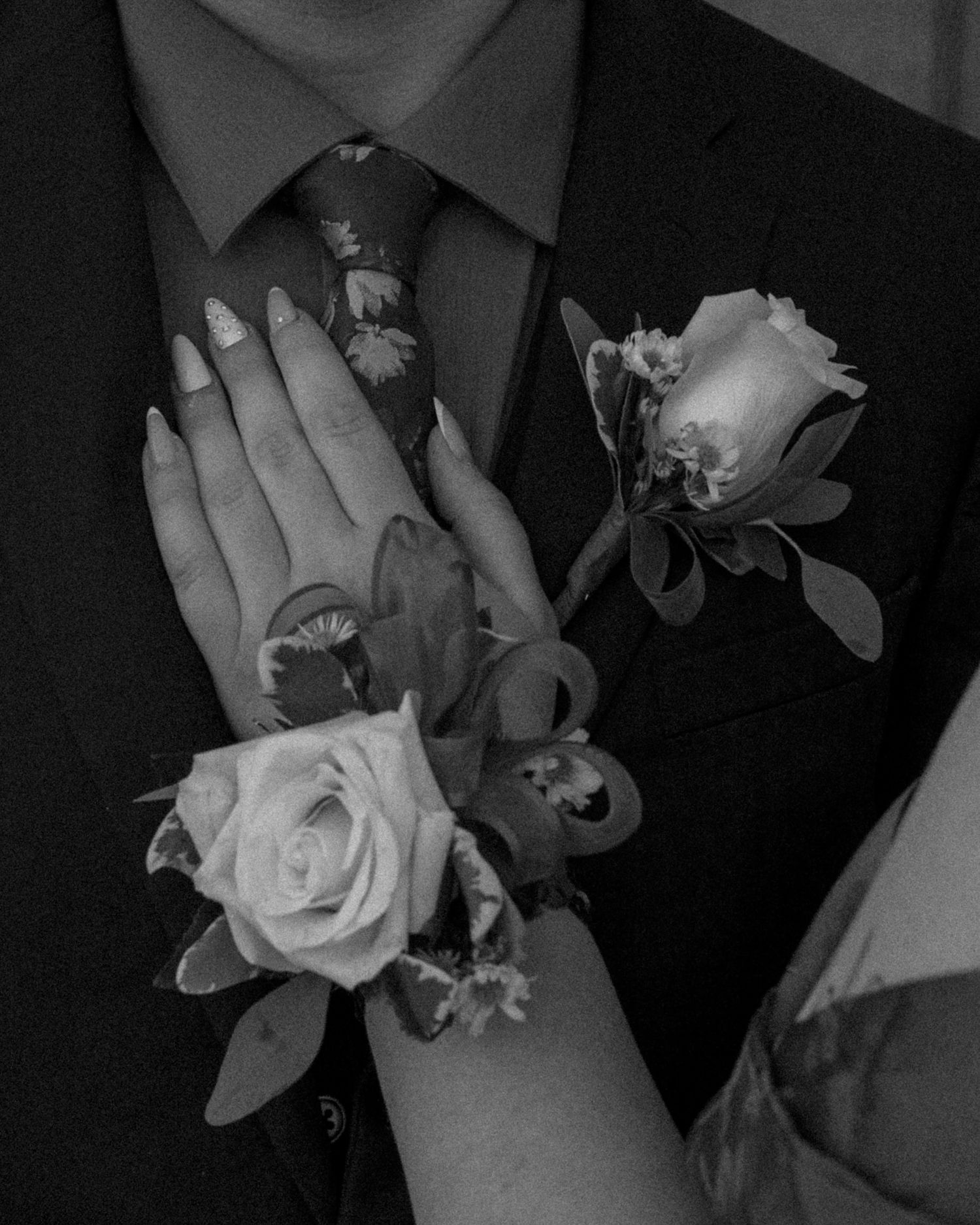 Black and white close-up of prom corsage and boutonniere with roses on couple in formal attire.