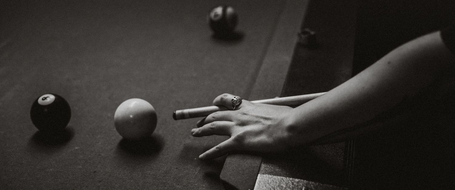 Black and white close-up of a hand on a pool table holding a cue stick near the cue ball and eight ball.