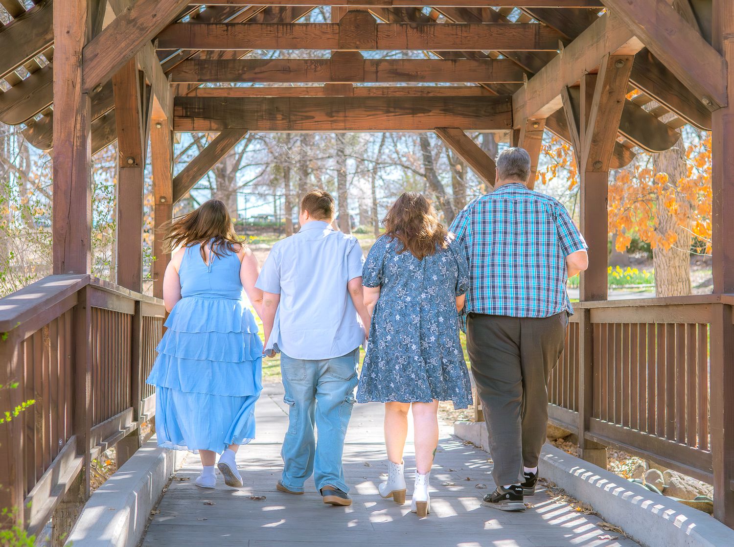 Family of four walks hand-in-hand through a wooden covered bridge surrounded by autumn foliage.