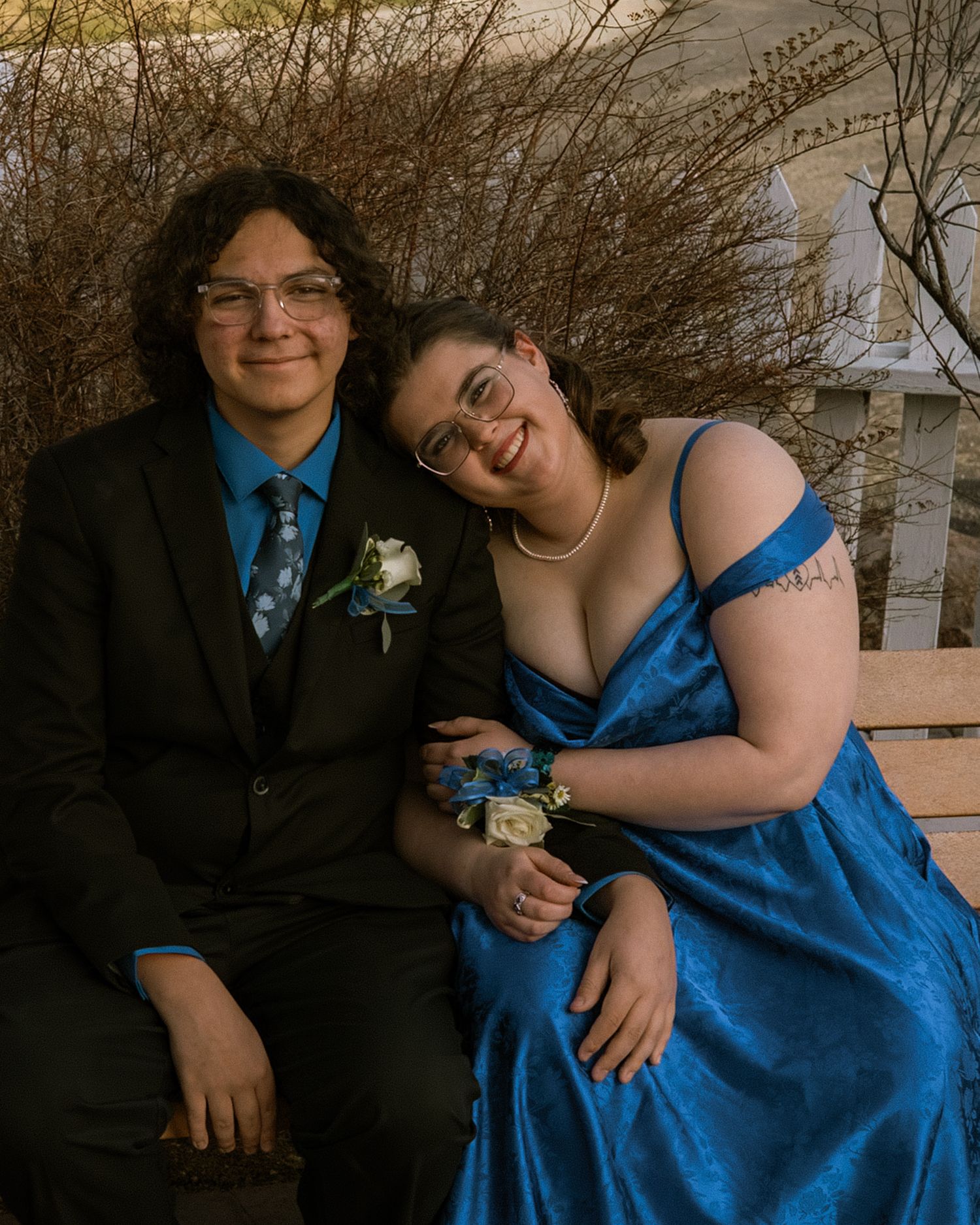 Teenage prom couple seated on bench, wearing matching blue accessories with corsage and boutonniere.